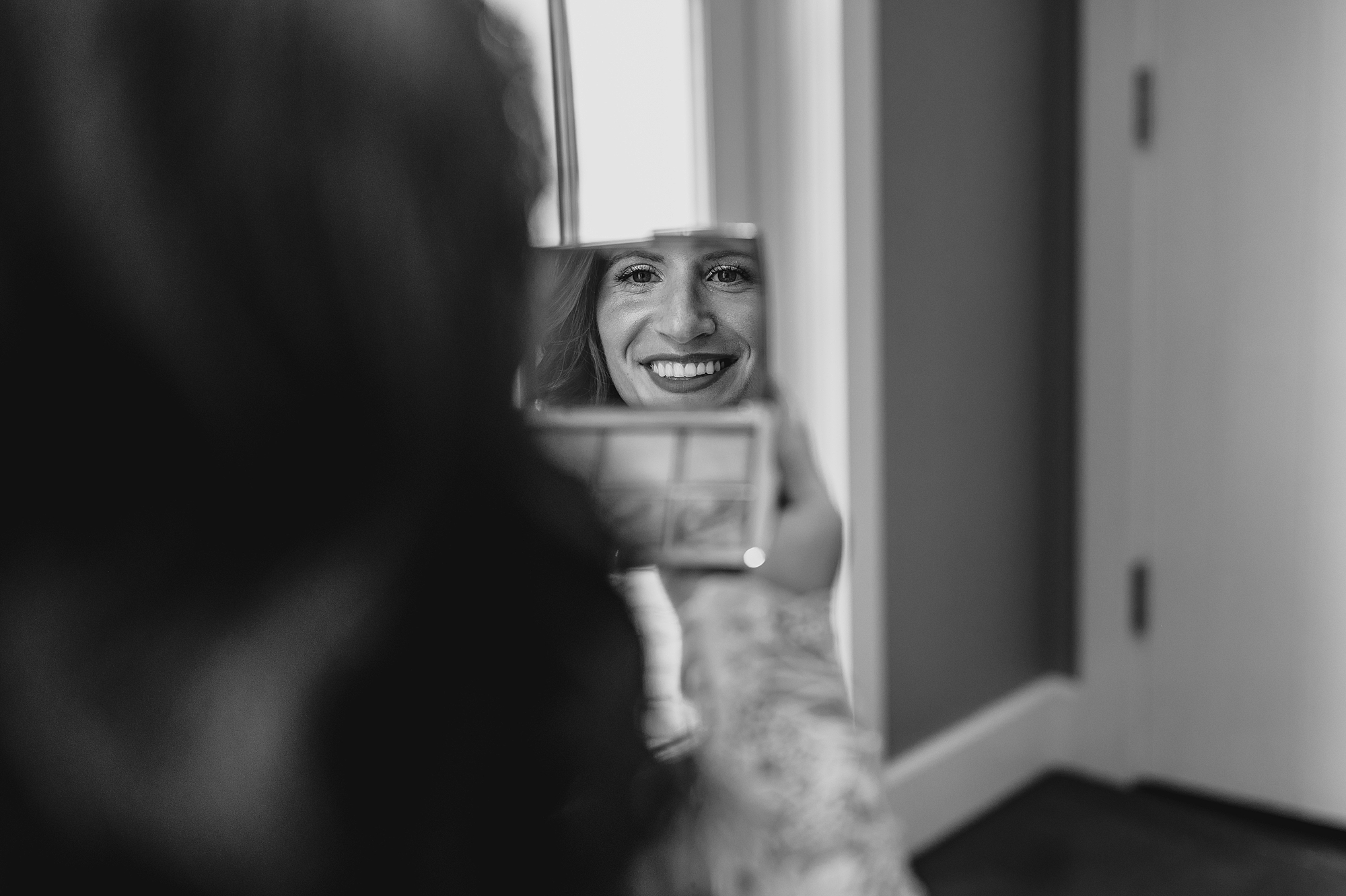 bride looks at reflection in small mirror in suite at the Ryland Inn
