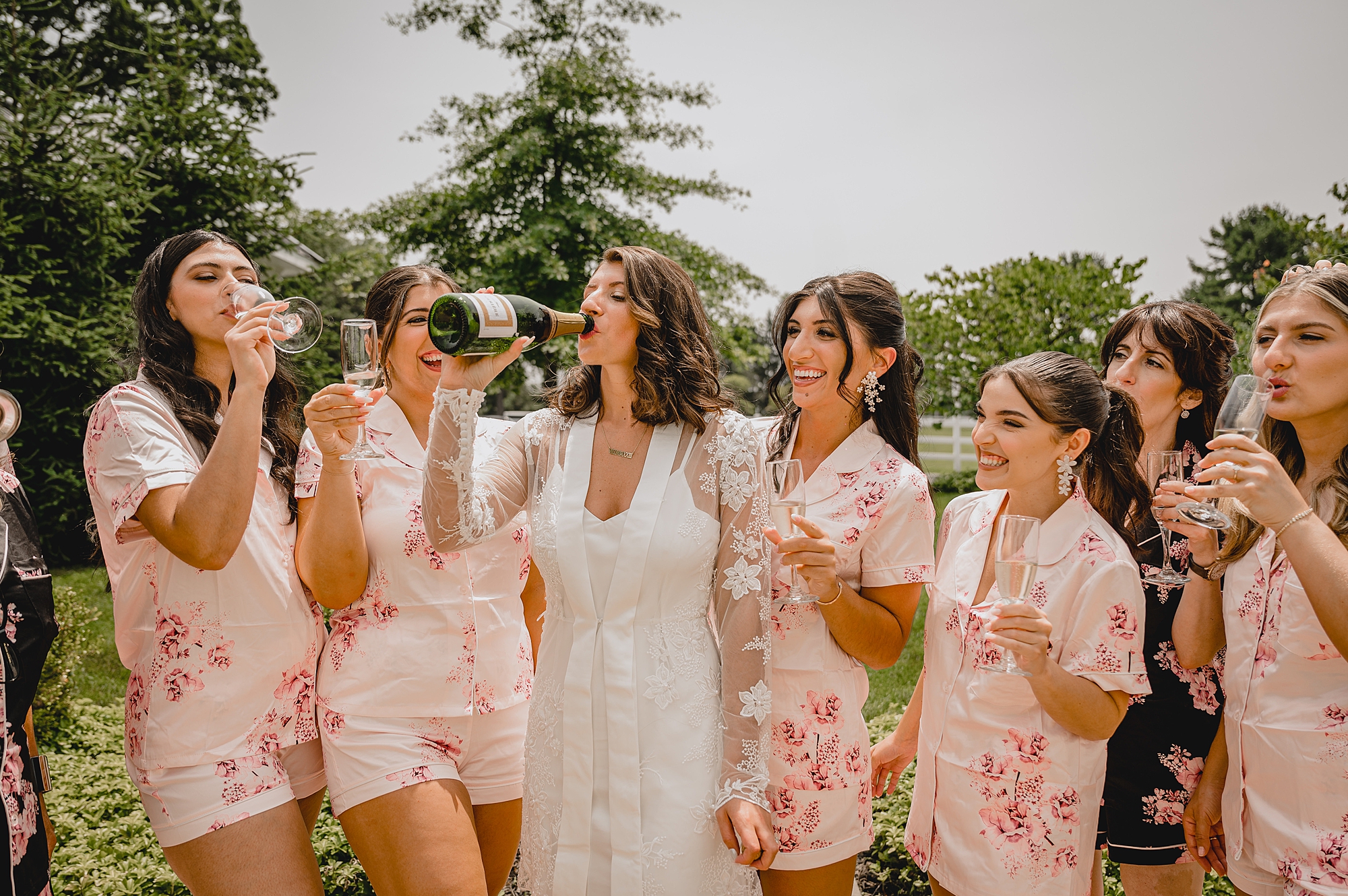 bride drinks from champagne bottle with bridesmaids