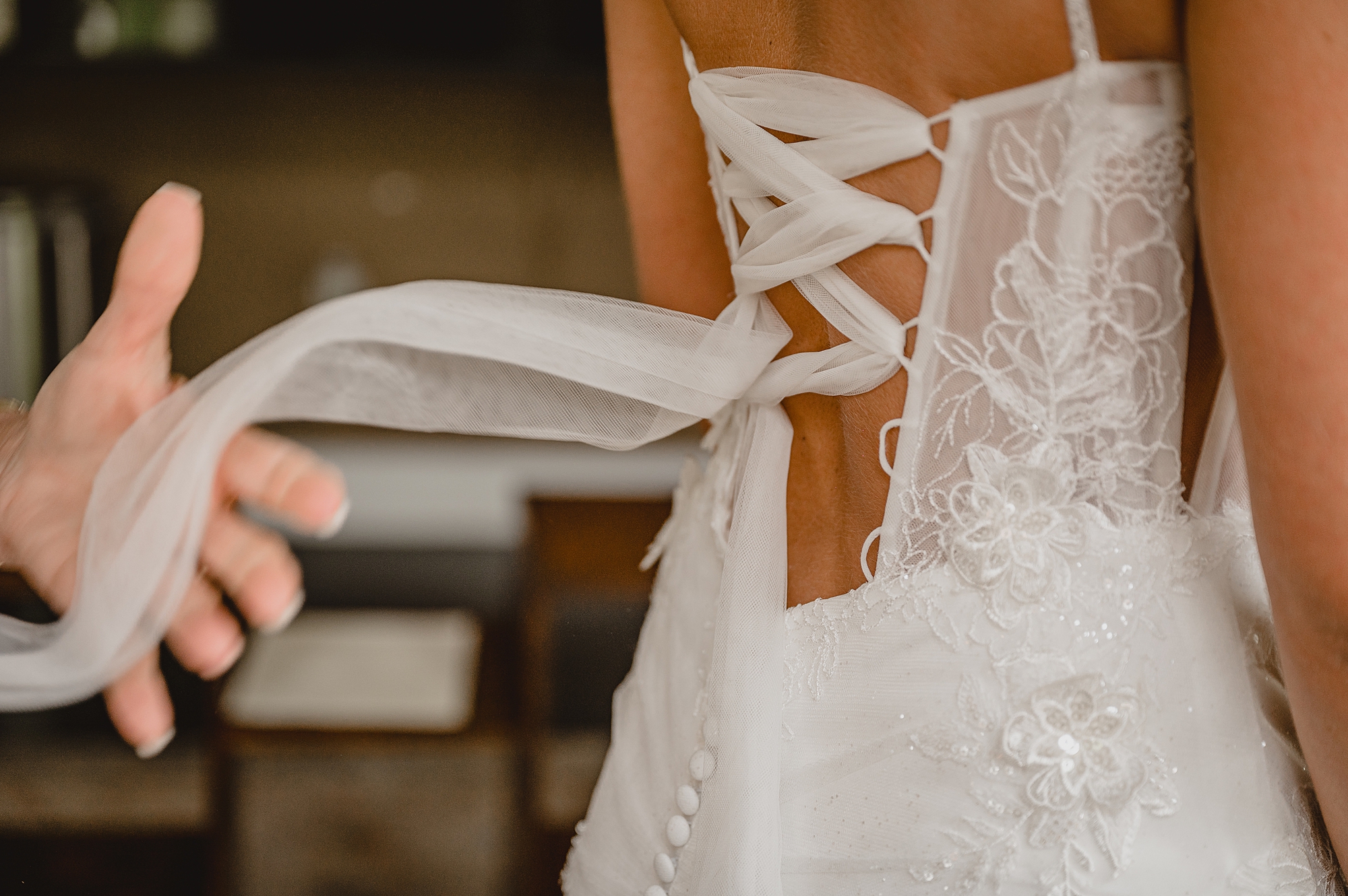 mother holds ribbon on back of wedding gown lacing up corset bodice