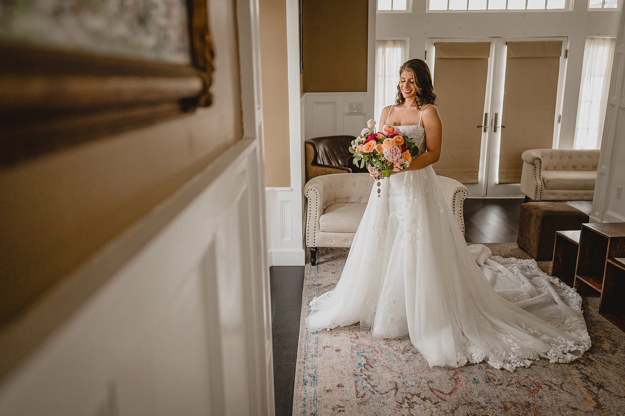 bride smiles standing in wedding gown with bouquet of pink and red flowers