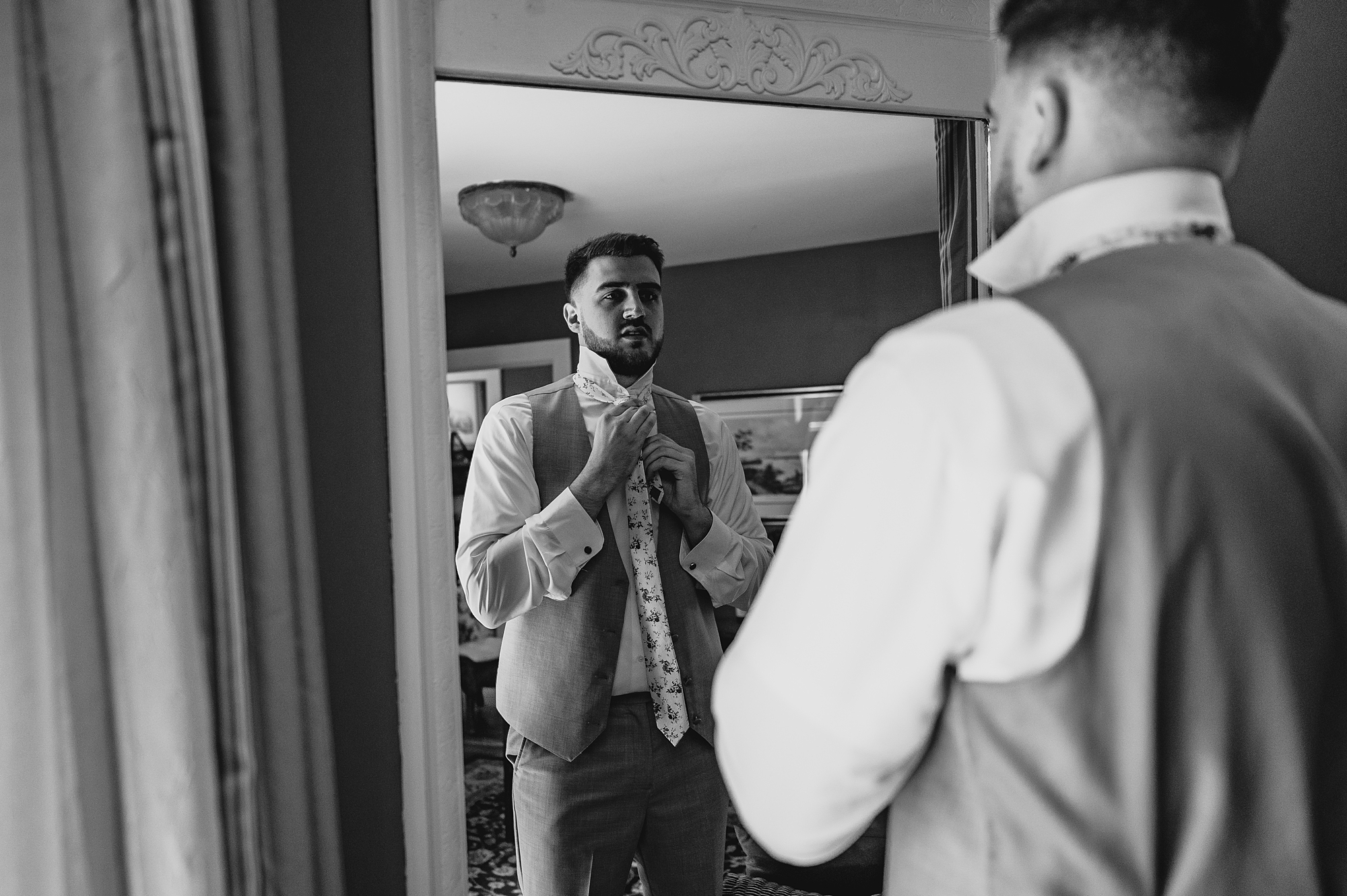 groom looks at self in mirror adjusting his tie