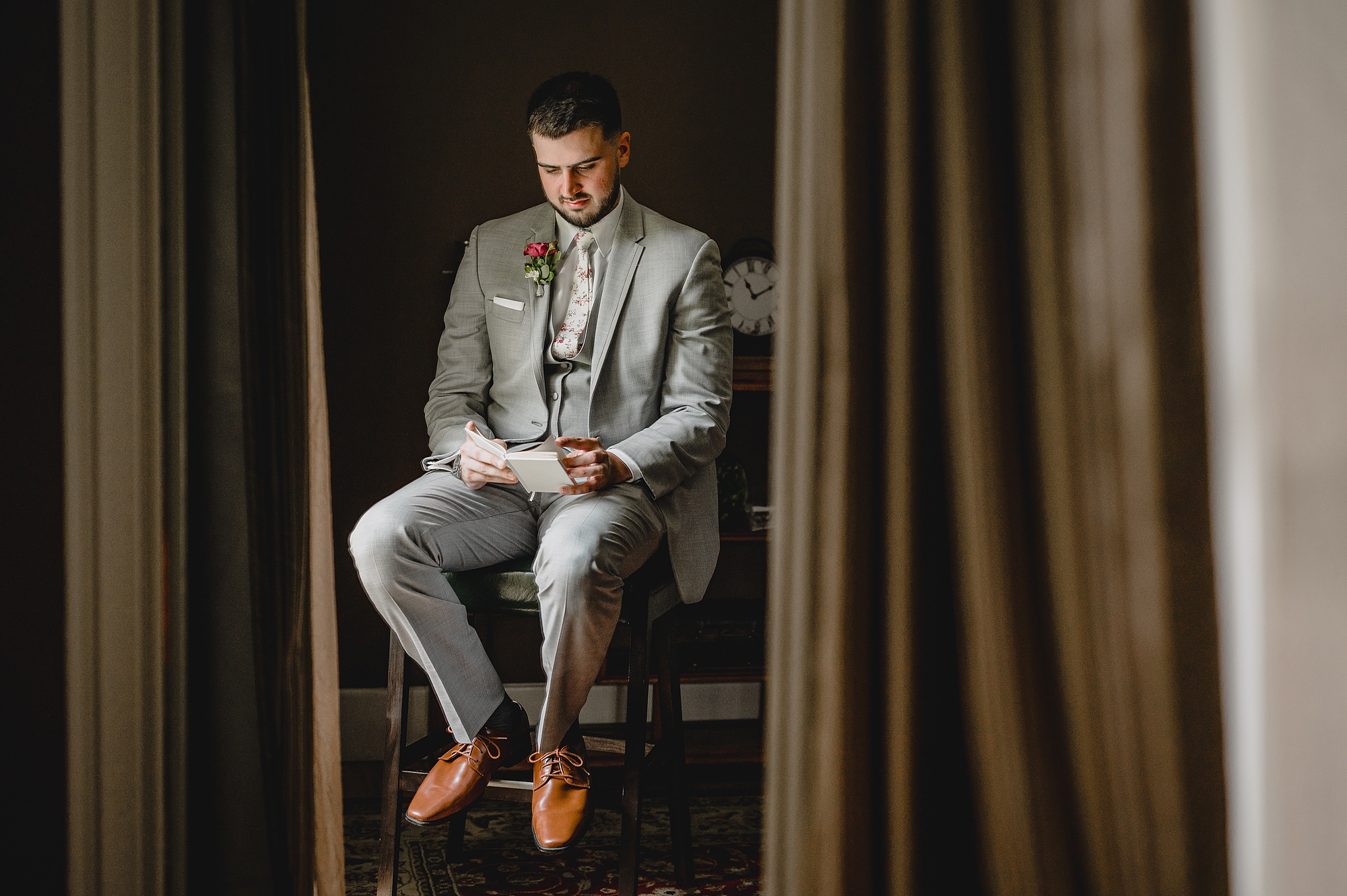 groom in grey suit sits to read vow booklet from bride