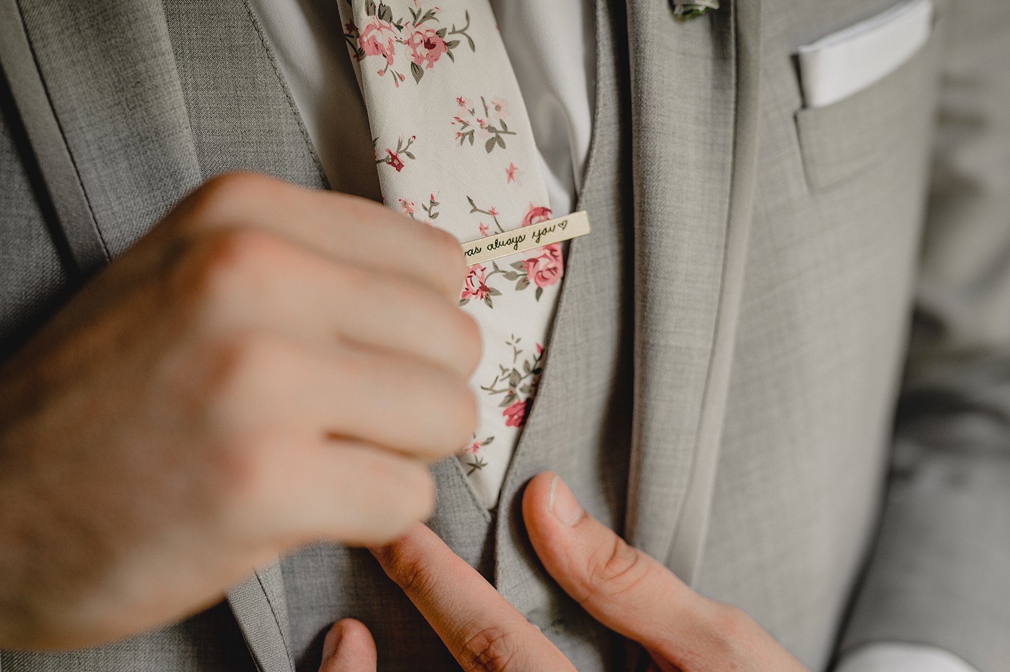 groom places tie clip on floral tie