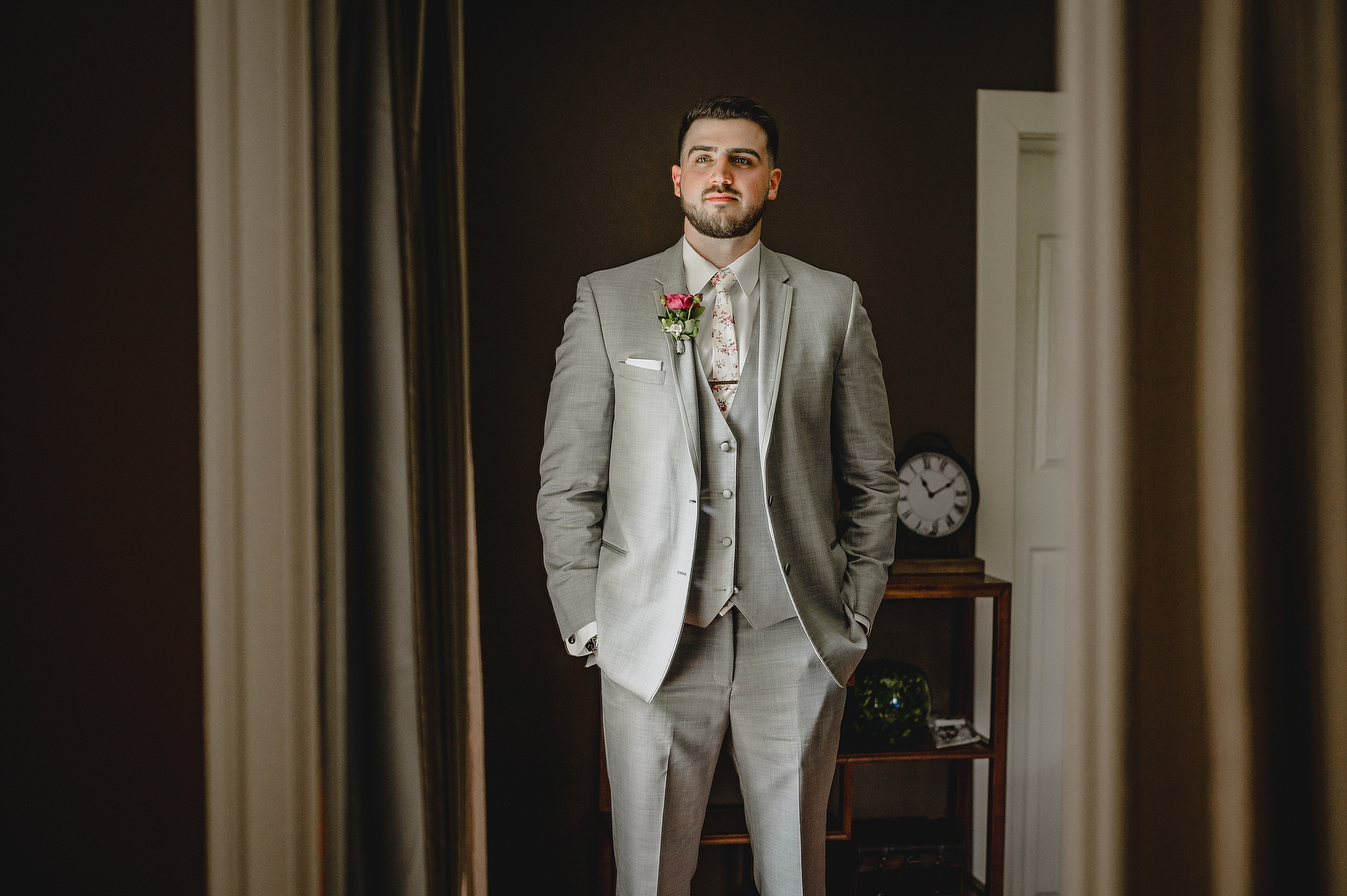 groom in grey suit stands with hands in his pockets in New Jersey room