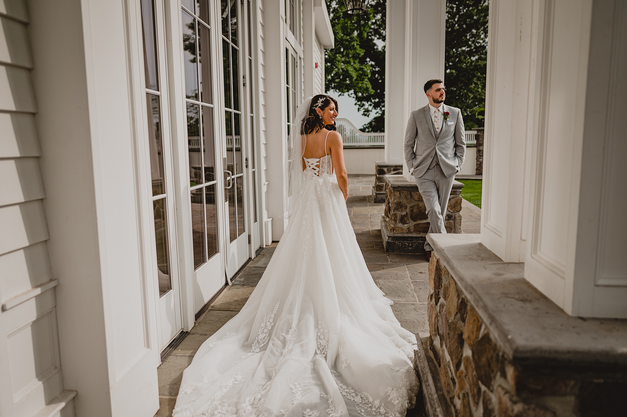 groom leans against pillar while bride looks out on lawn