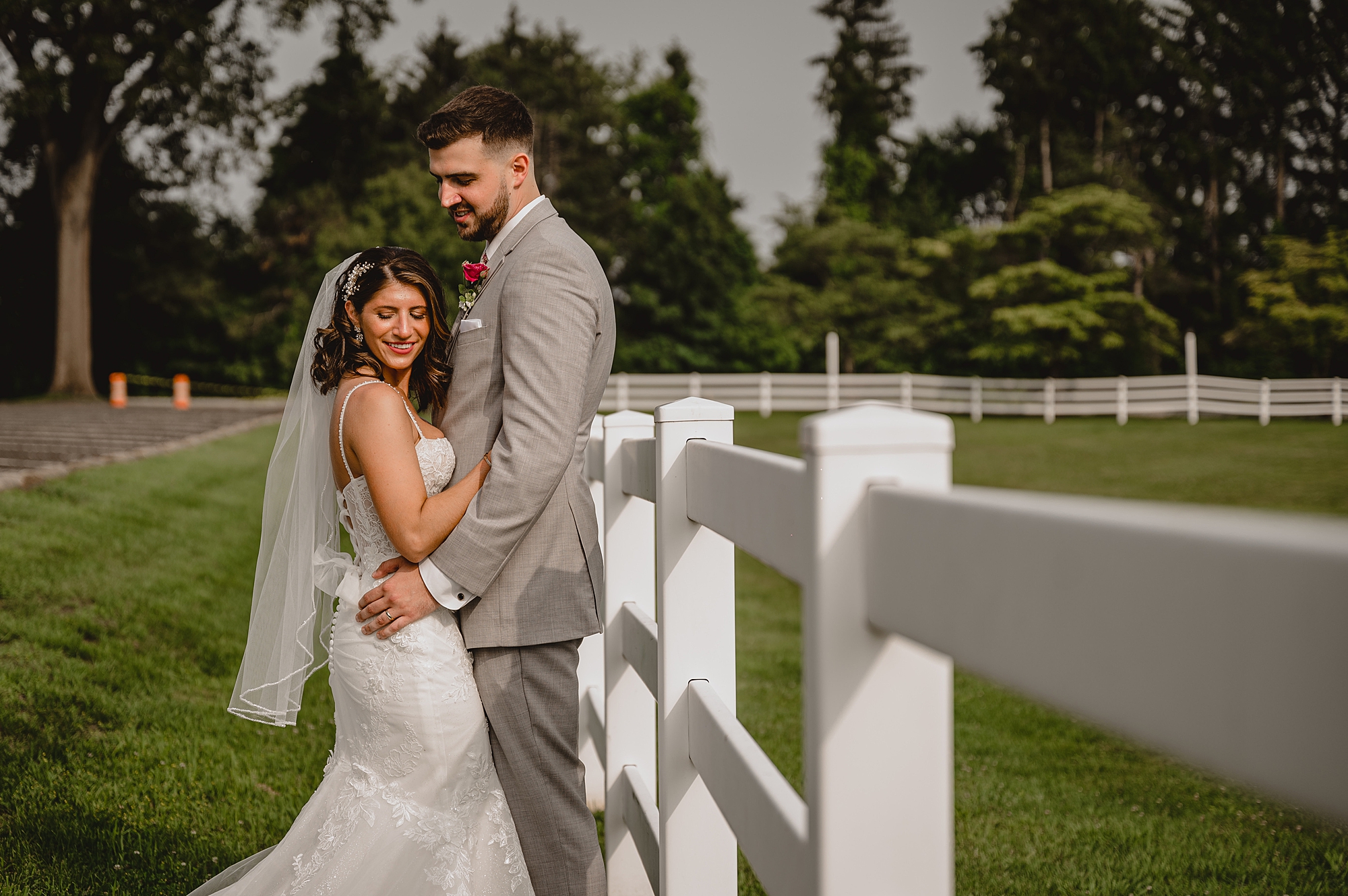 bride and groom hug leaning against white fence at the Ryland Inn