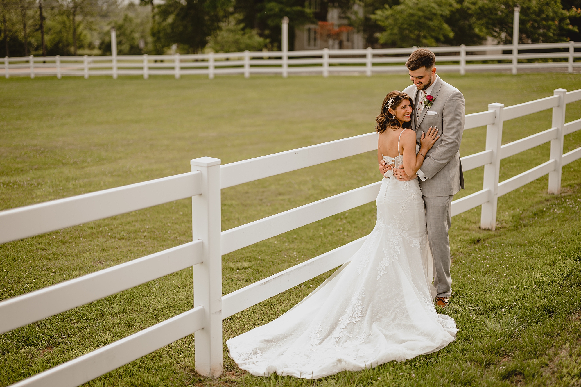 bride and groom hug against white wooden fence at the Ryland Inn