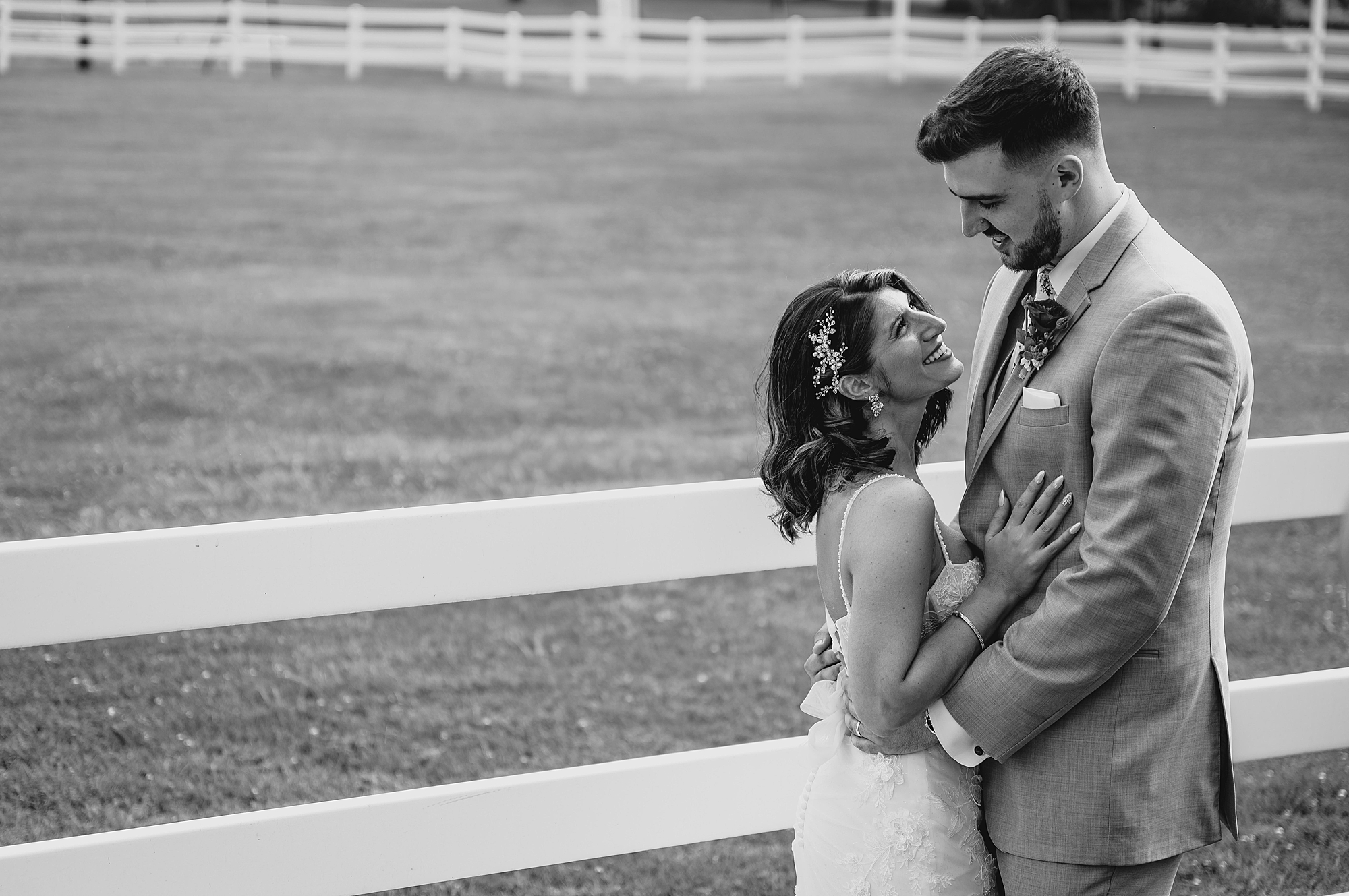 bride smiles up at groom during portraits along fence line at the Ryland Inn