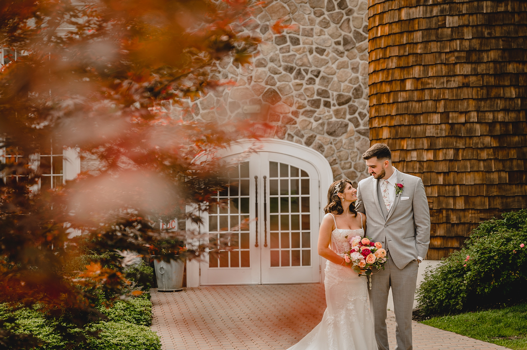 bride smiles up at groom with leaves in the foreground of the photo
