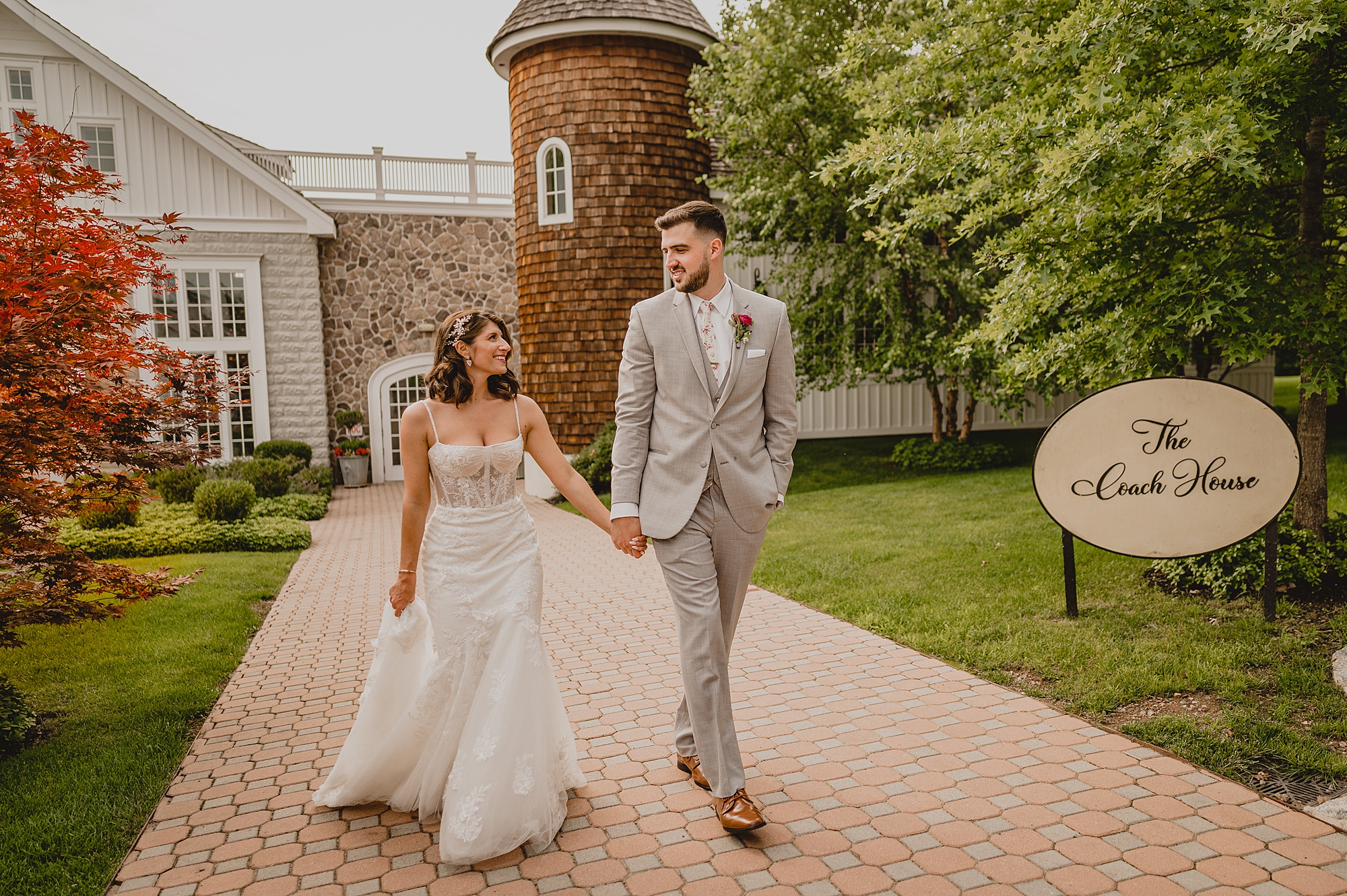 groom in grey suit holds bride's hand walking on driveway at the Ryland Inn