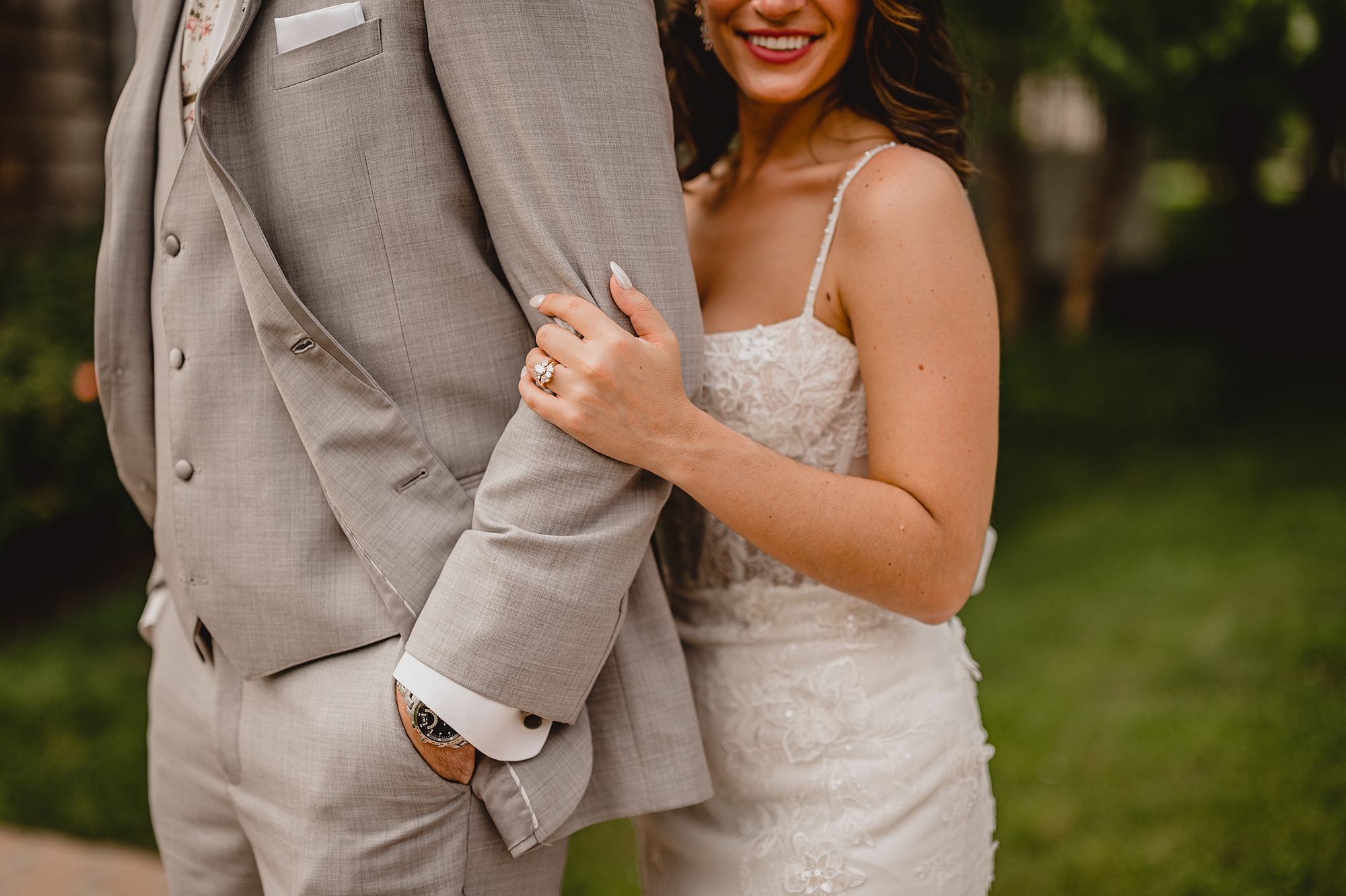 bride holds groom's arm standing behind him showing off her ring