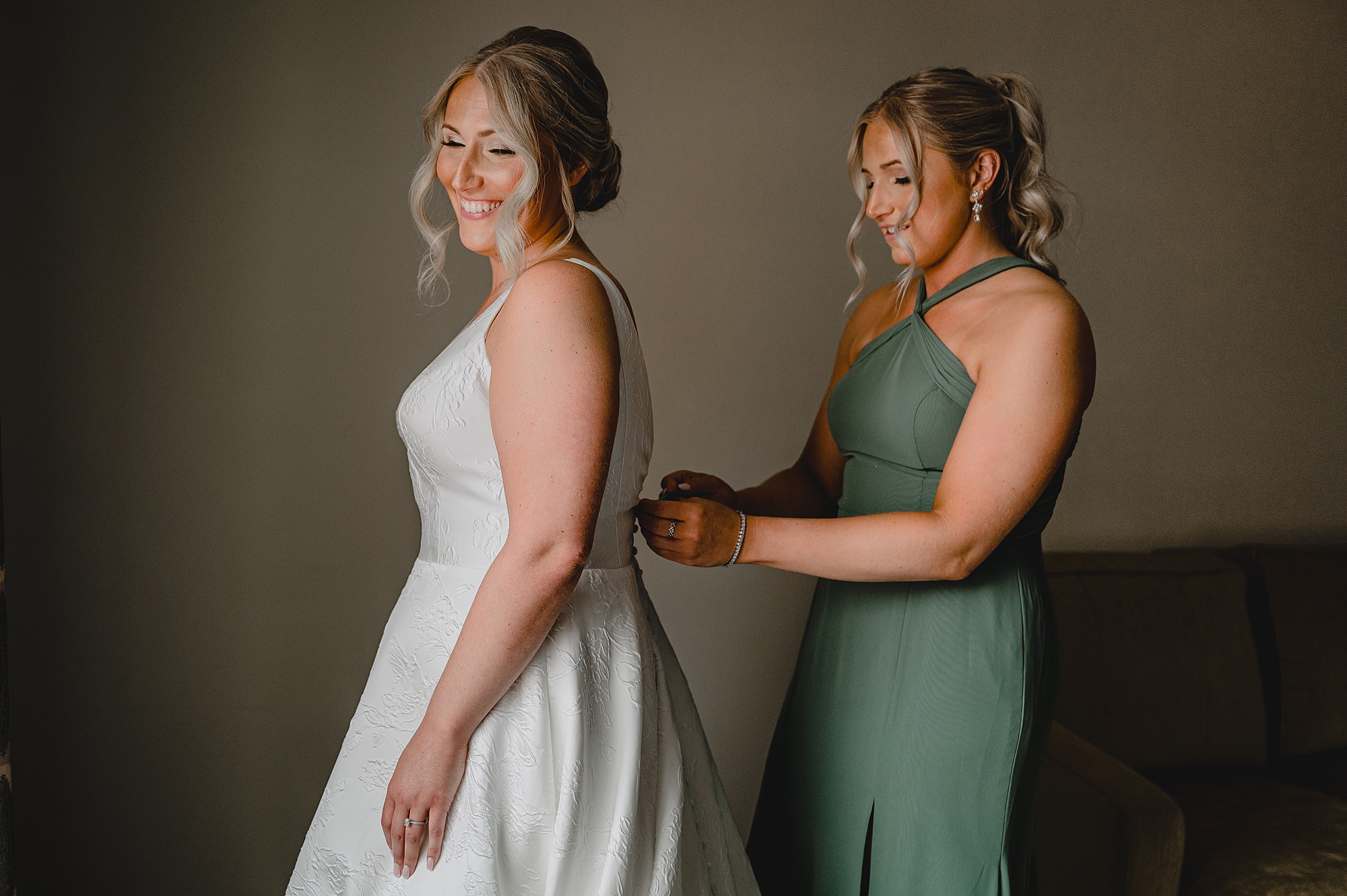 bridesmaid in sage green gown buttons up bride's dress