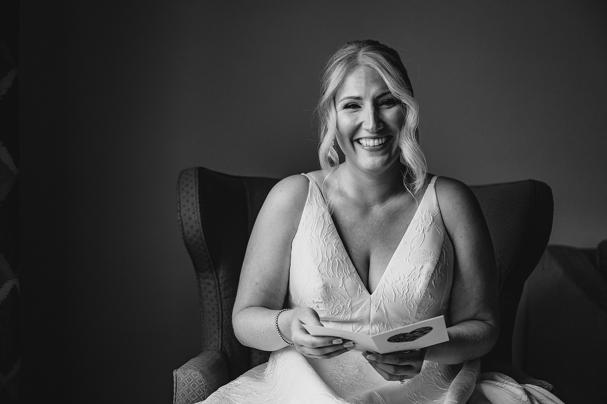 black and white photo of bride laughing holding card on wedding morning