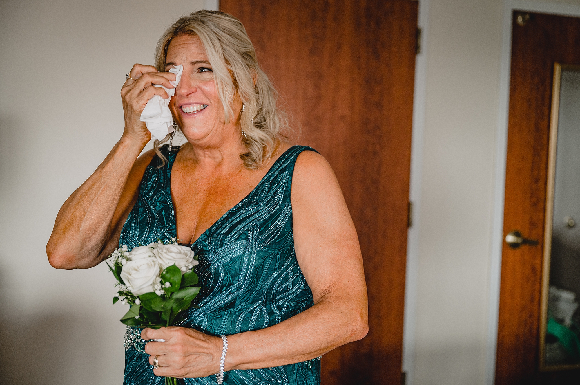 mother in teal gown wipes eyes during wedding day prep in hotel