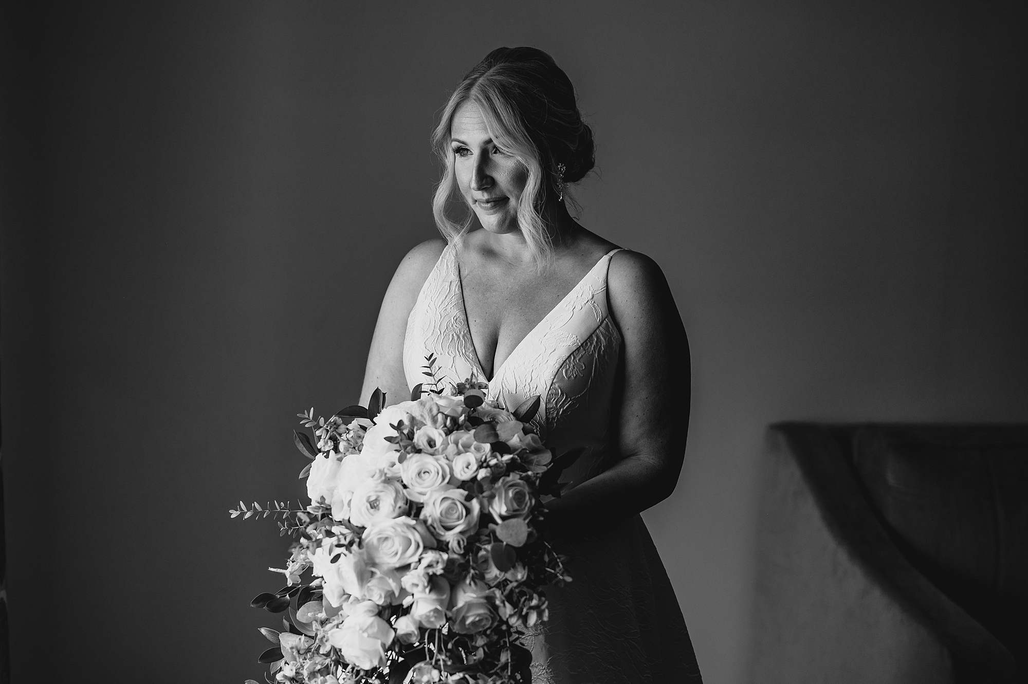 bride holds bouquet of flowers in front of v-neck of wedding gown