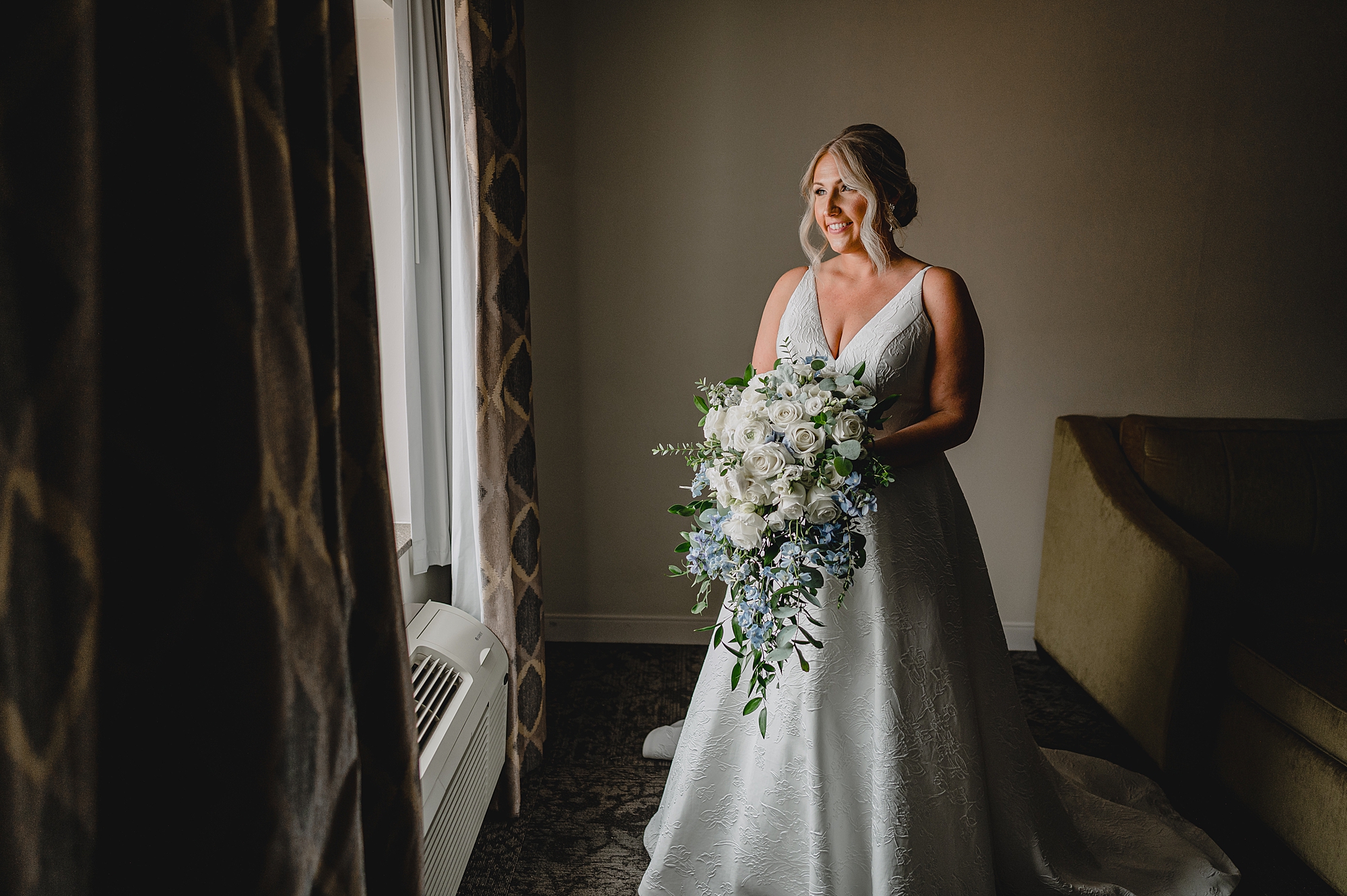 bride smiles holding cascading bouquet of white and blue flowers
