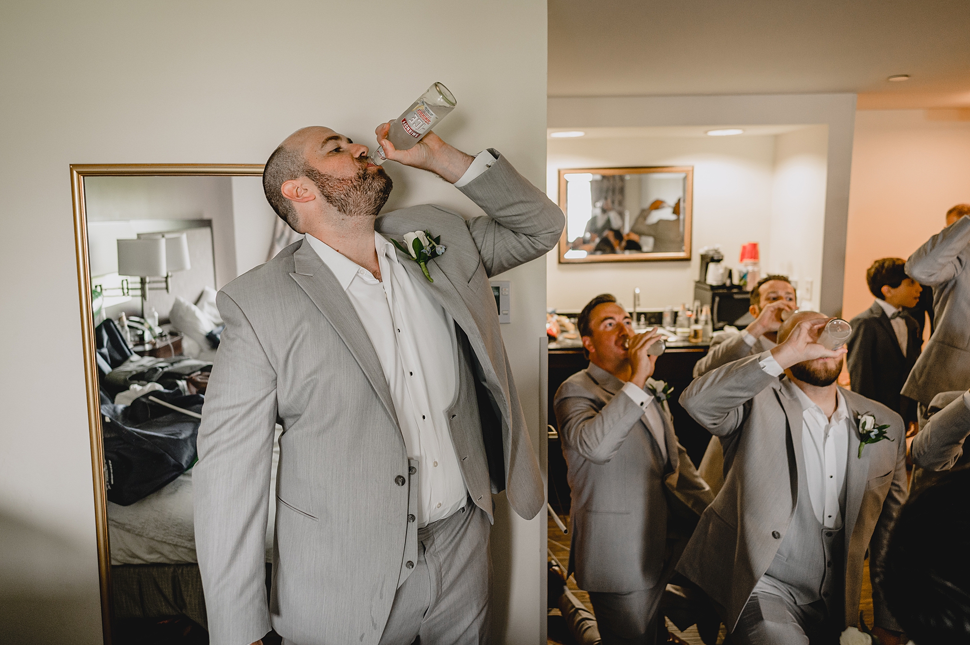 groom drinks alcohol straight from bottle in grey suit