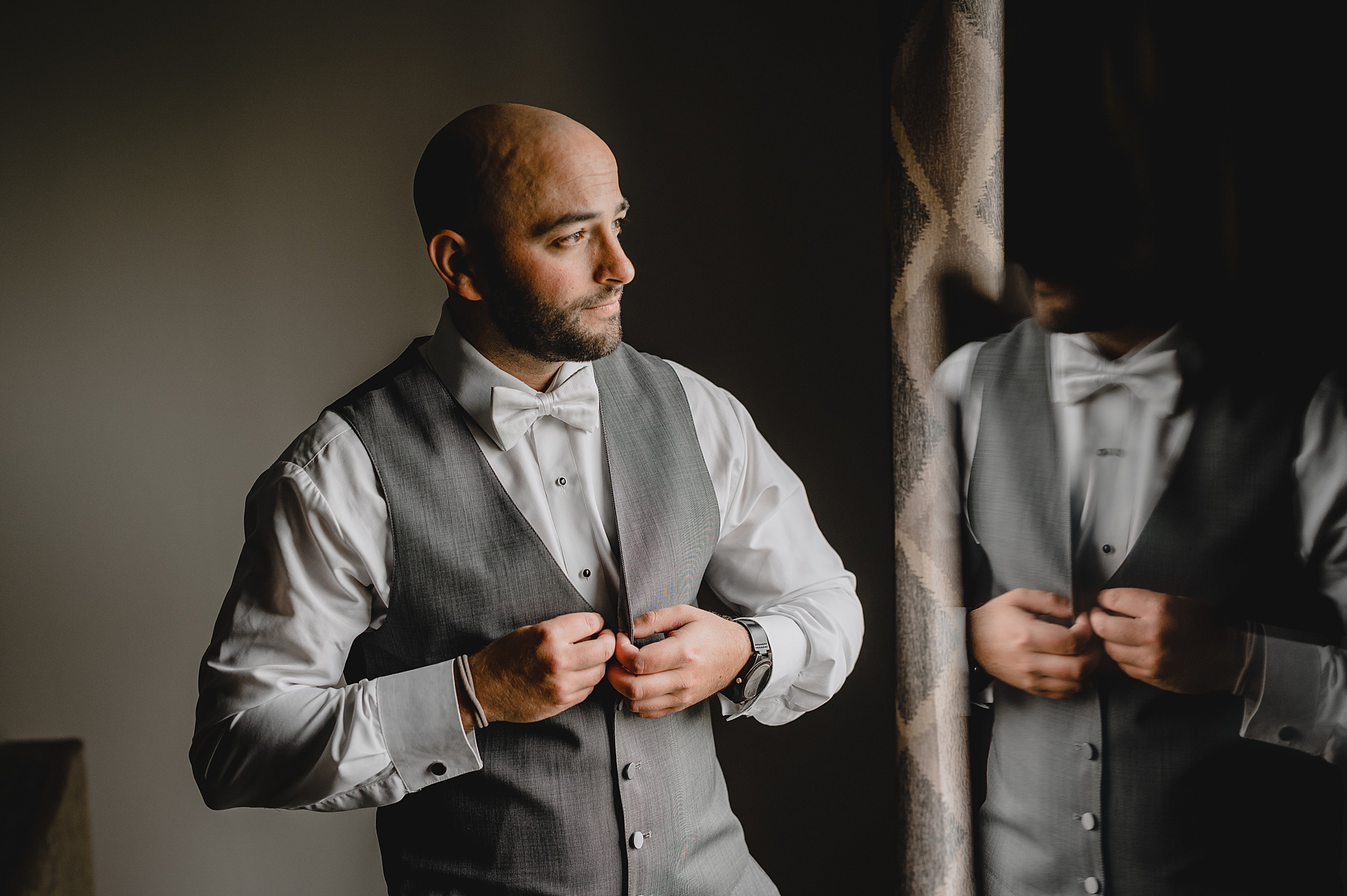 groom buttons up grey vest looking out window