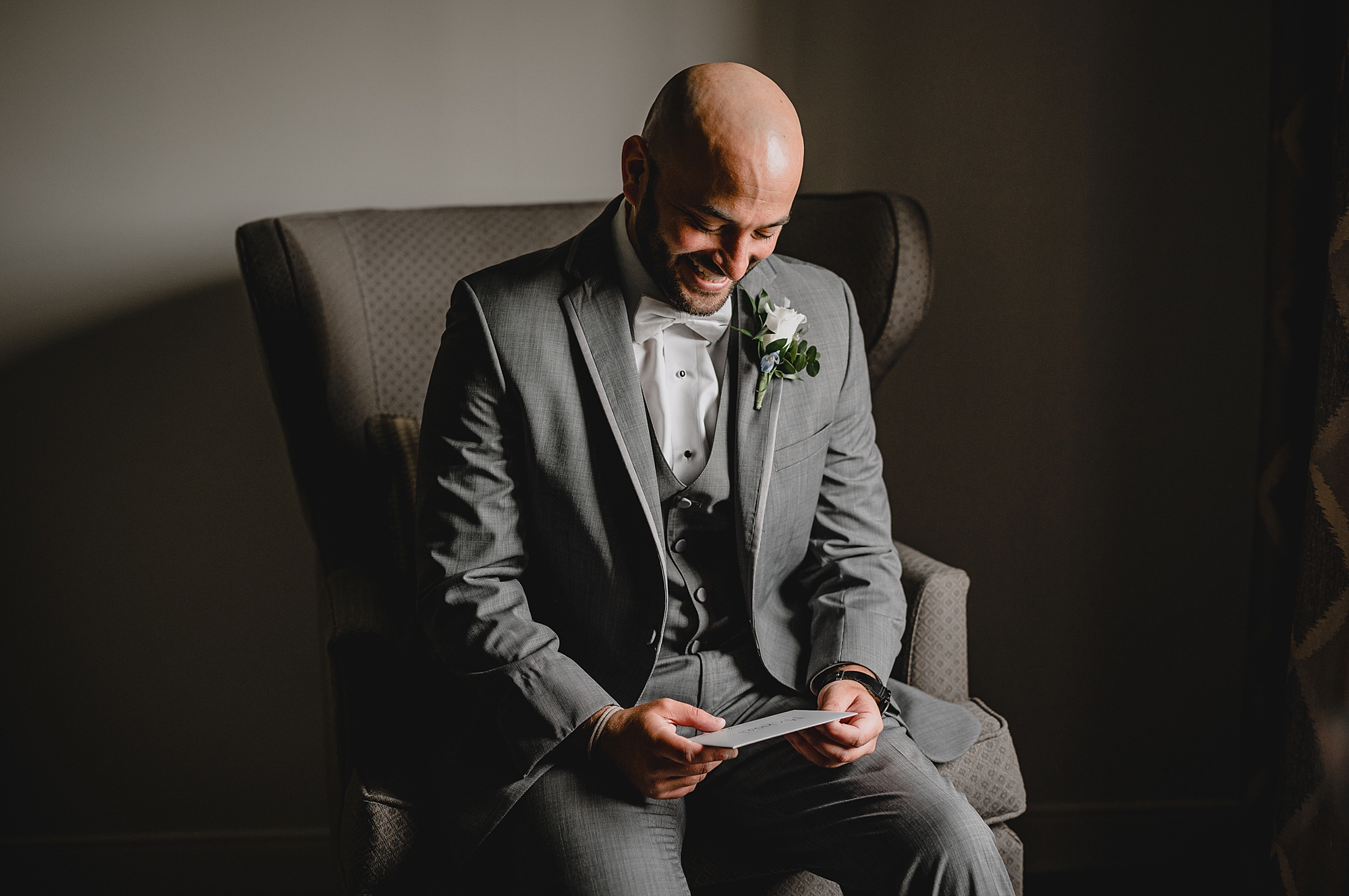 groom grins down at card in his hand from the bride