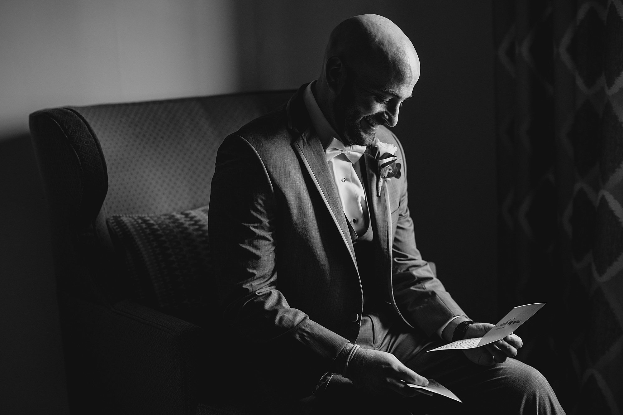 groom reads card sitting on leather chair