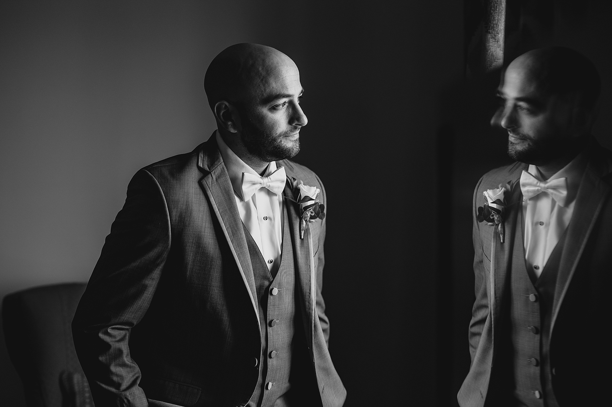 groom looks out window with reflection of his suit