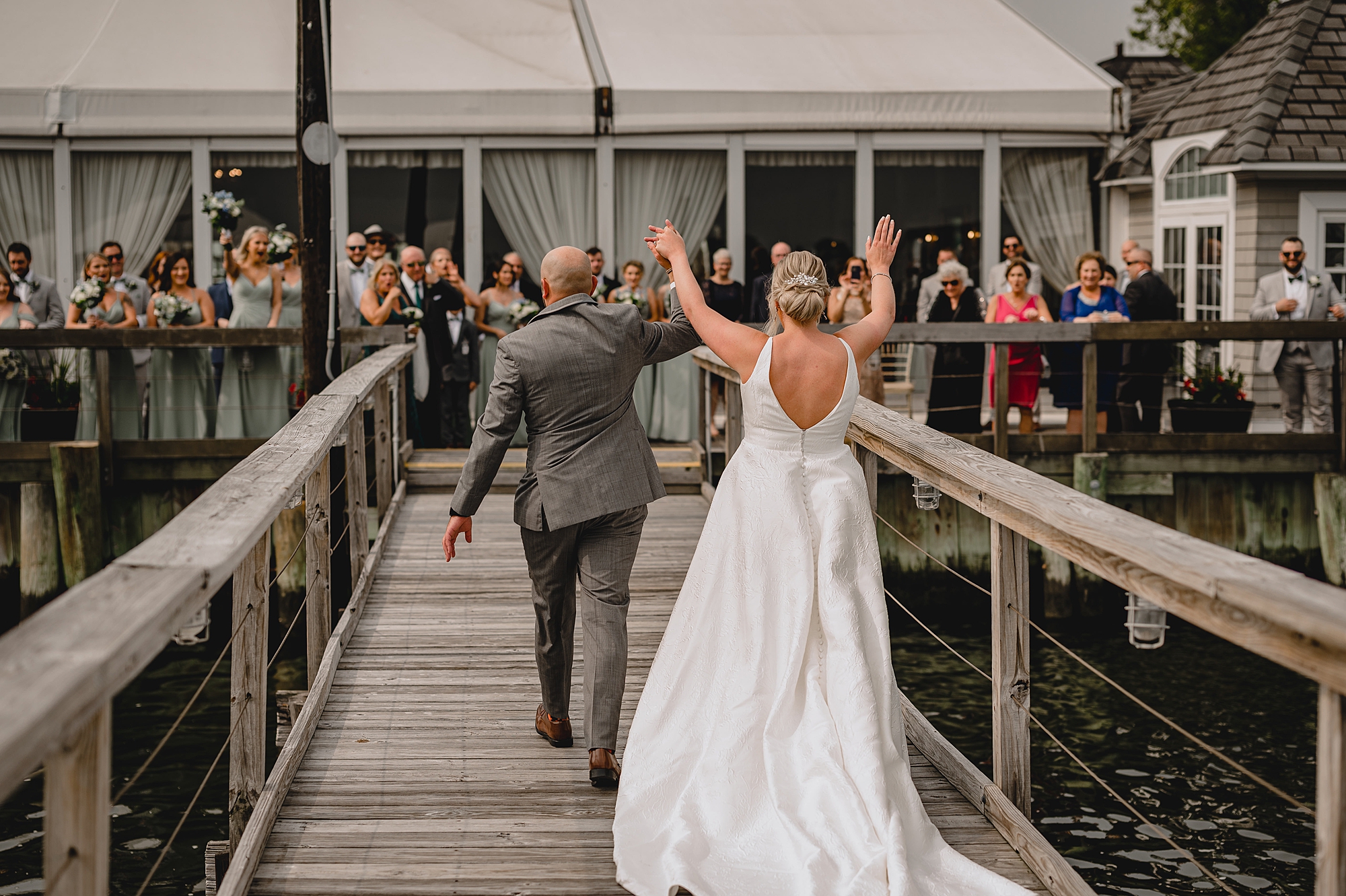 bride and groom cheer walking up dock towards family at Bridgeview Yacht Club