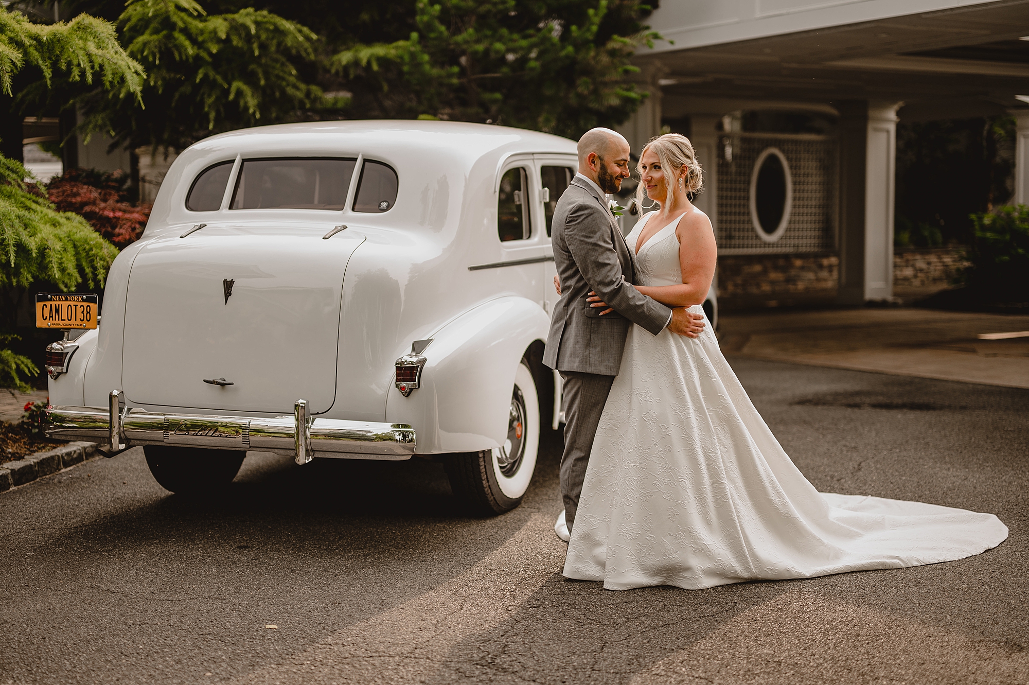 groom hugs bride around middle posing by classic white rolls Royce
