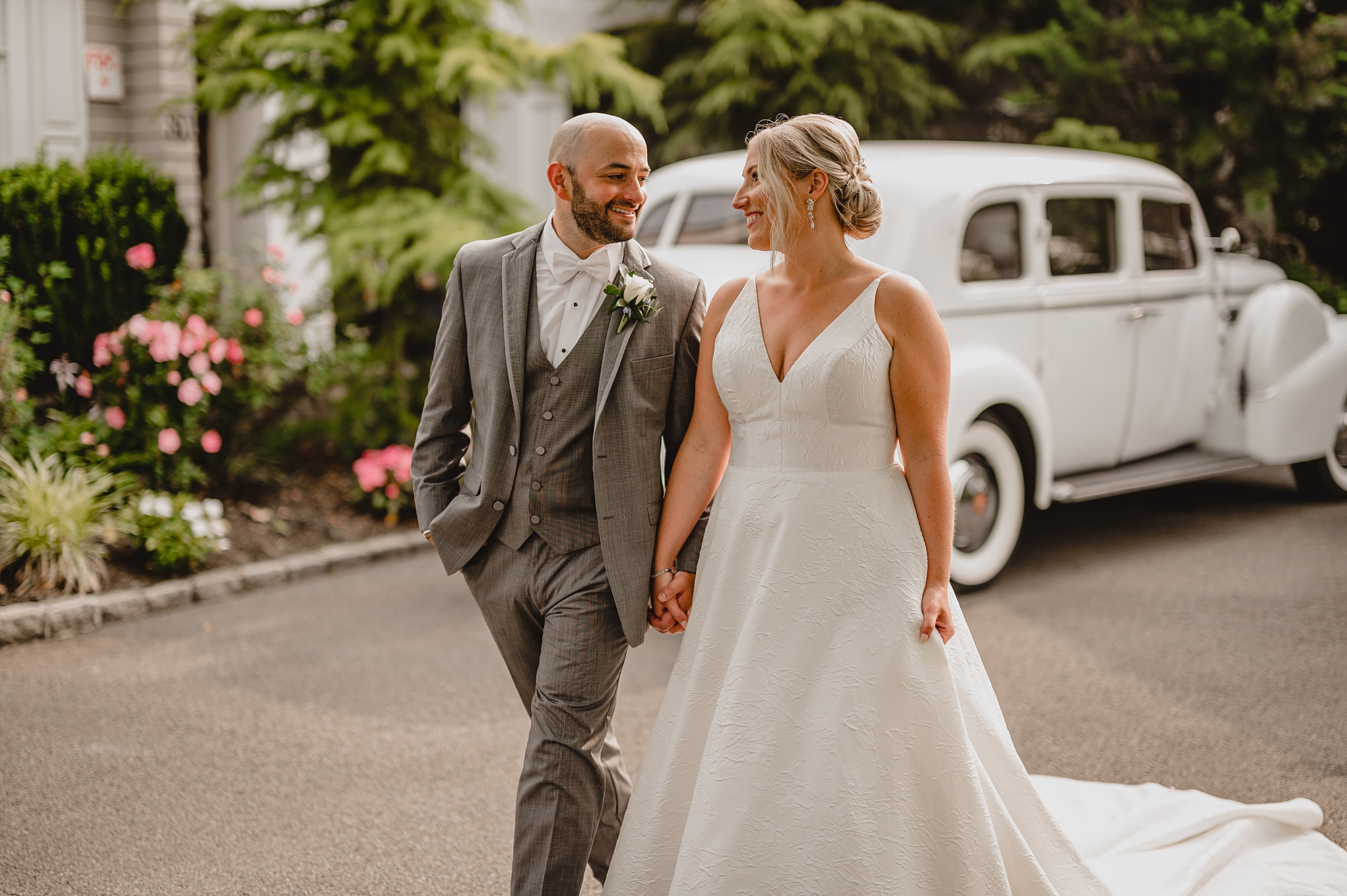 bride and groom hold hands walking past white vintage car