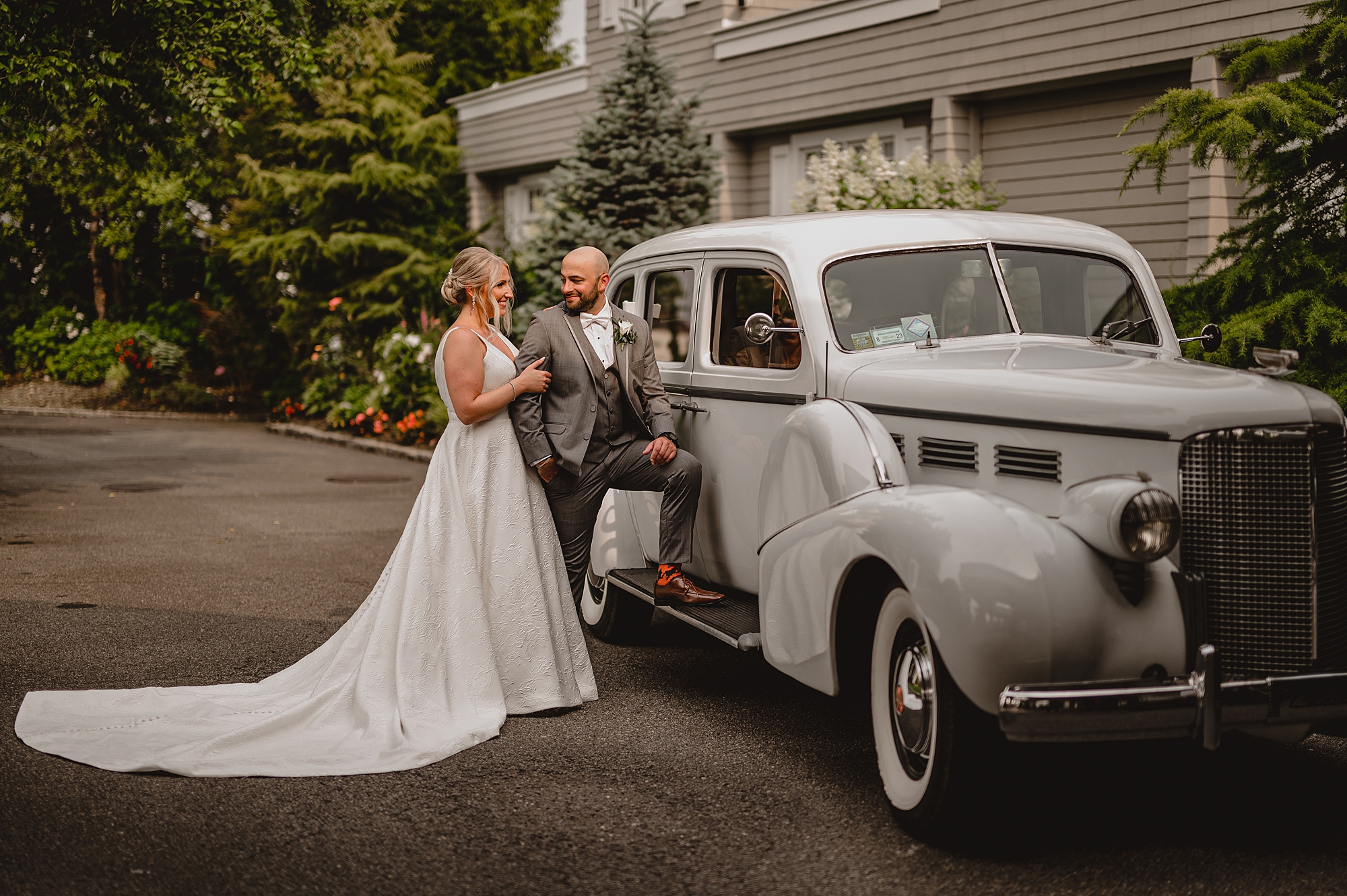 groom puts one leg on running board of white car while looking back at bride