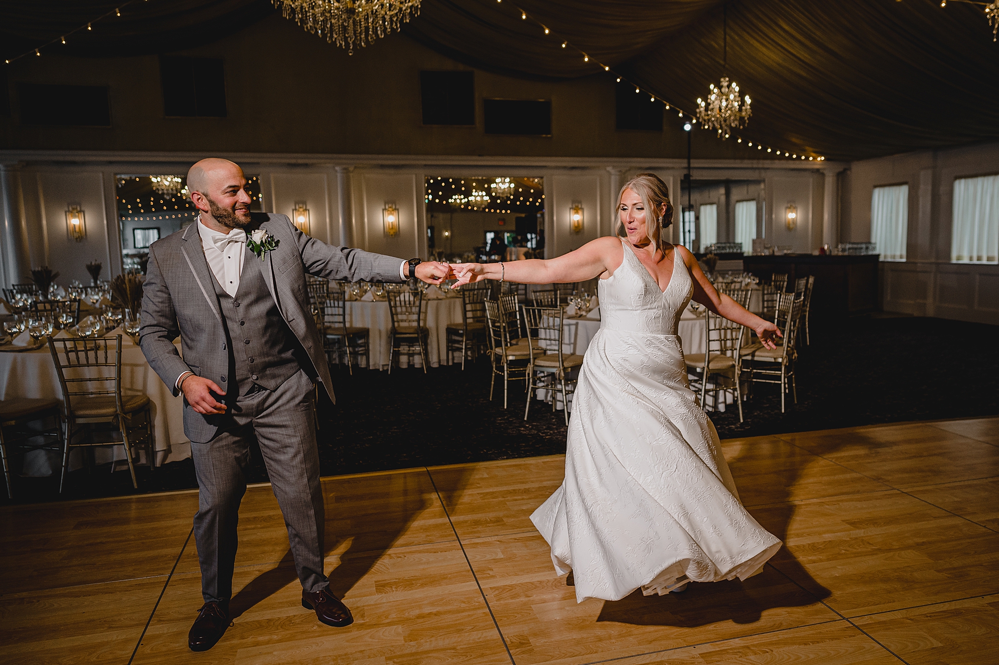 groom twirls bride on dance floor inside Bridgeview Yacht Club