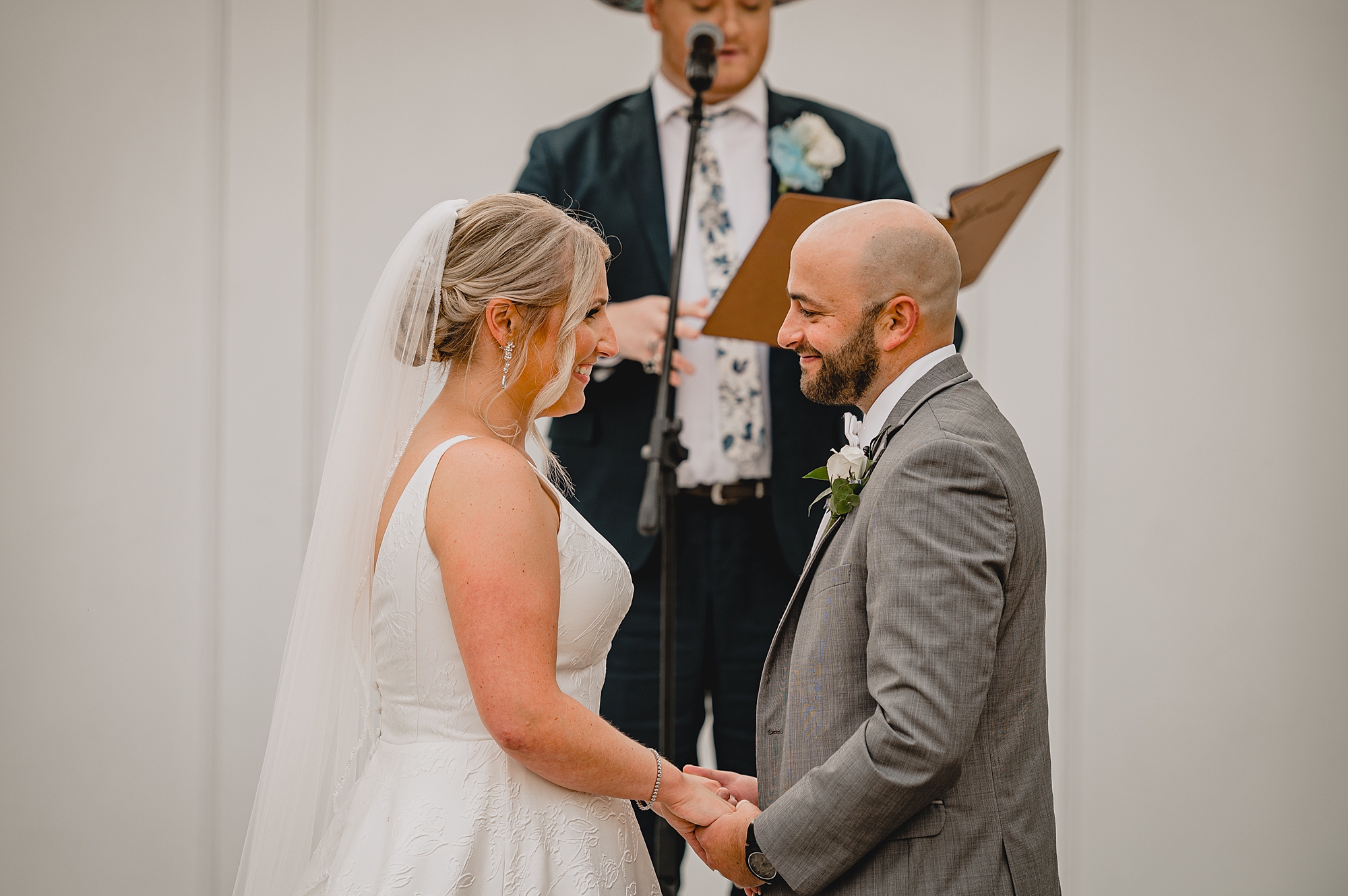 bride and groom smile holding hands during wedding ceremony at Bridgeview Yacht Club