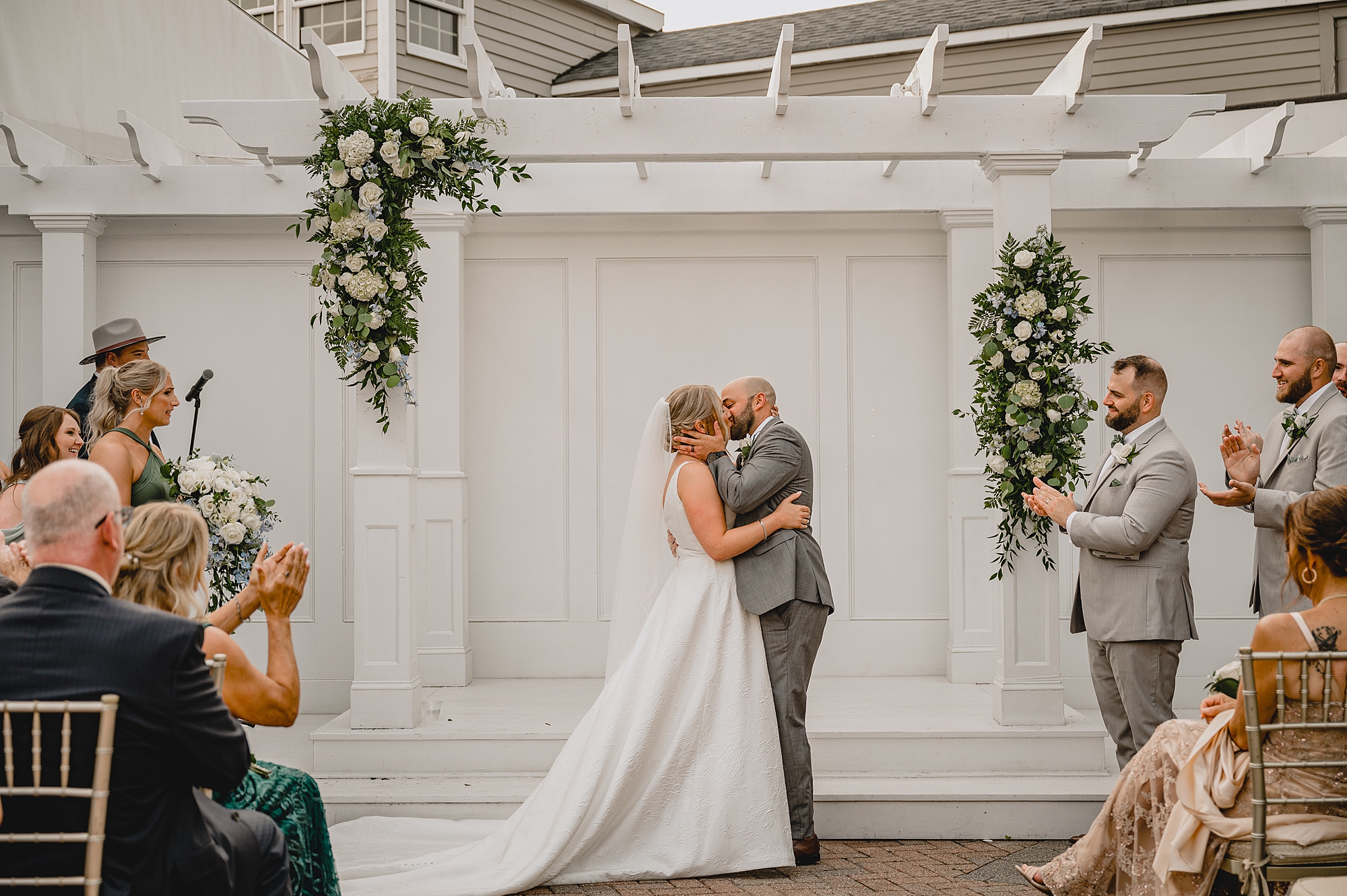 newlyweds kiss under wooden arbor outside Bridgeview Yacht Club after ceremony