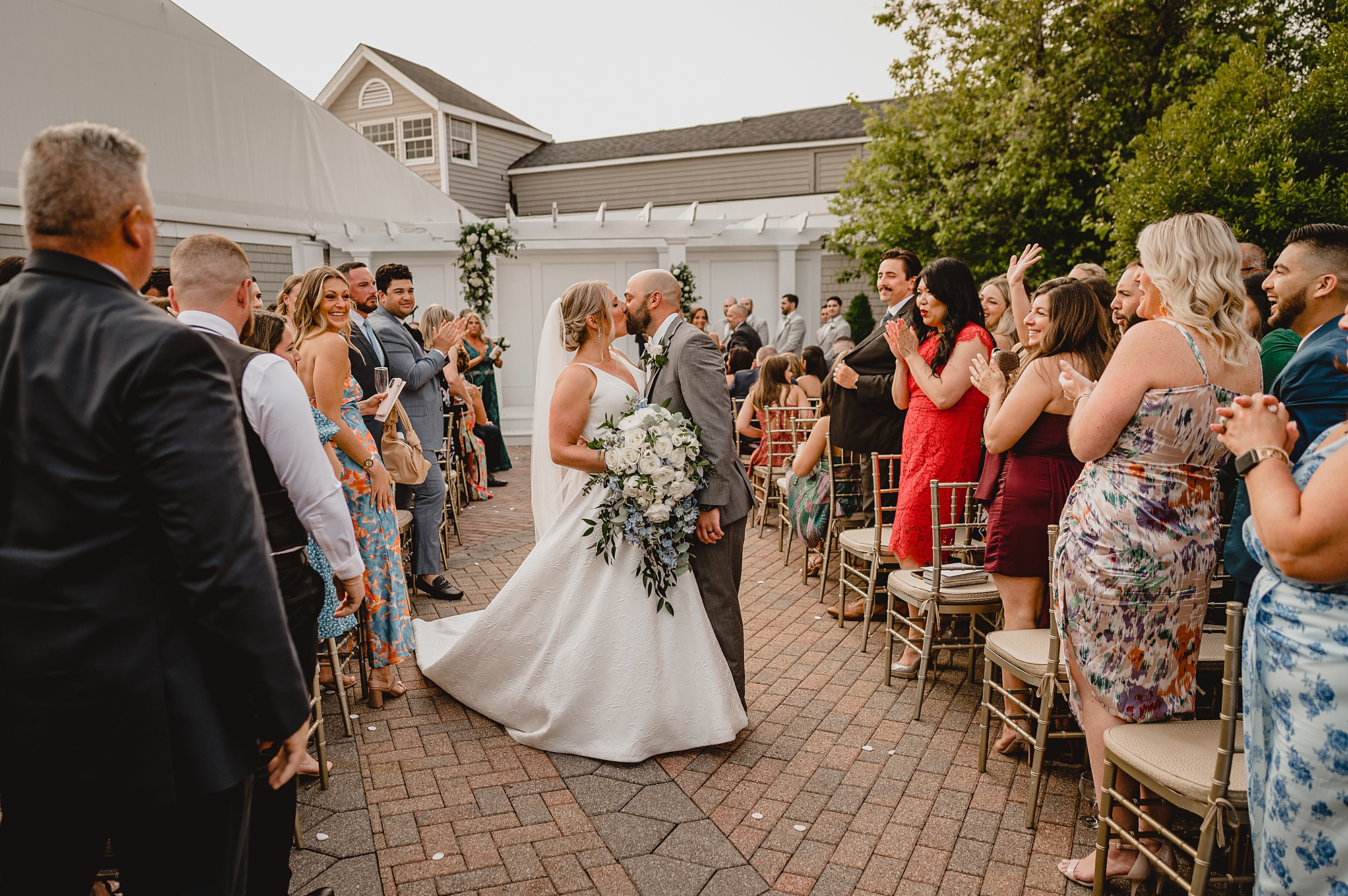 newlyweds kiss in aisle after wedding ceremony in garden of Bridgeview Yacht Club