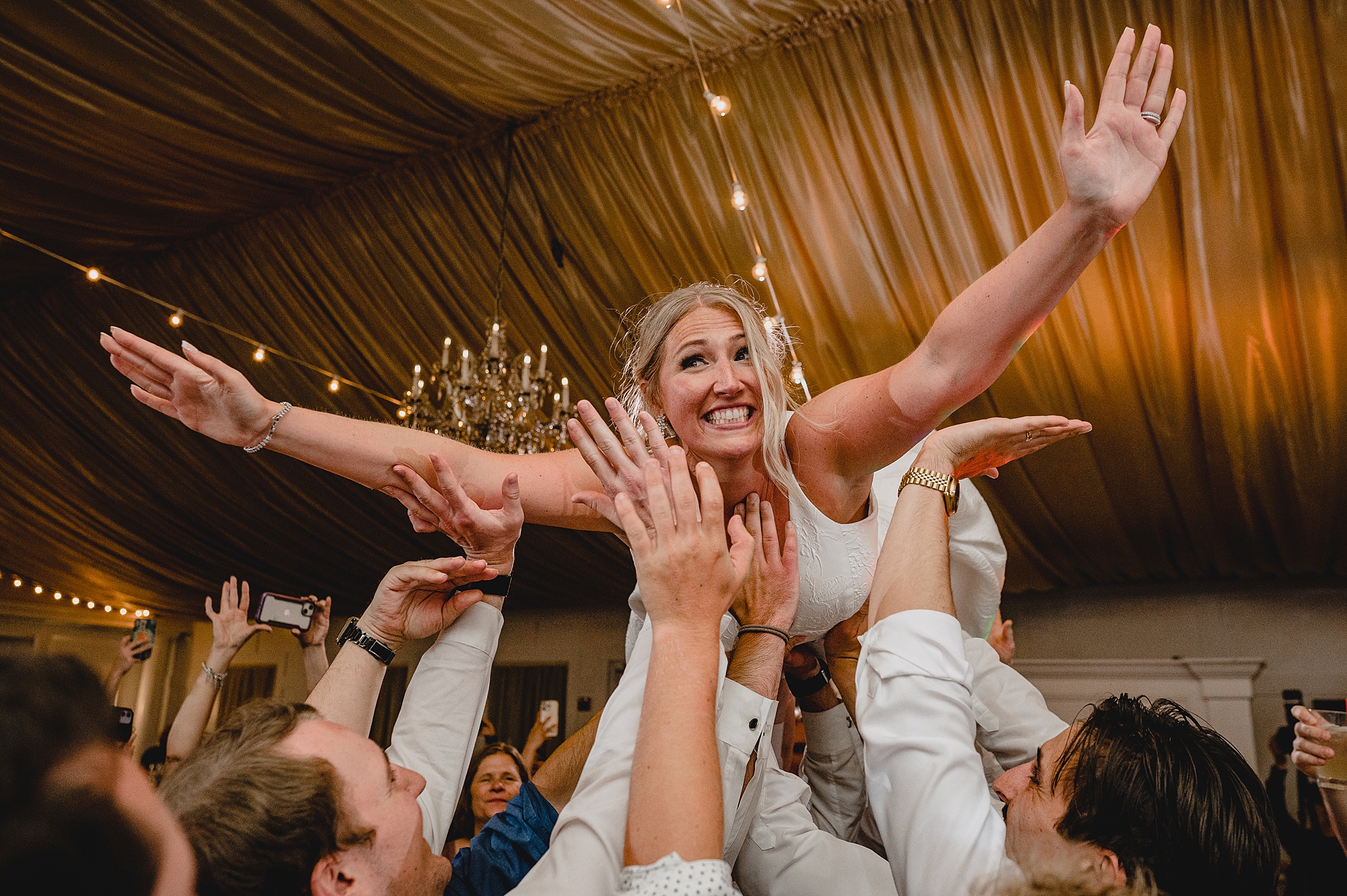 bride jumps on wedding guests holding her in the air