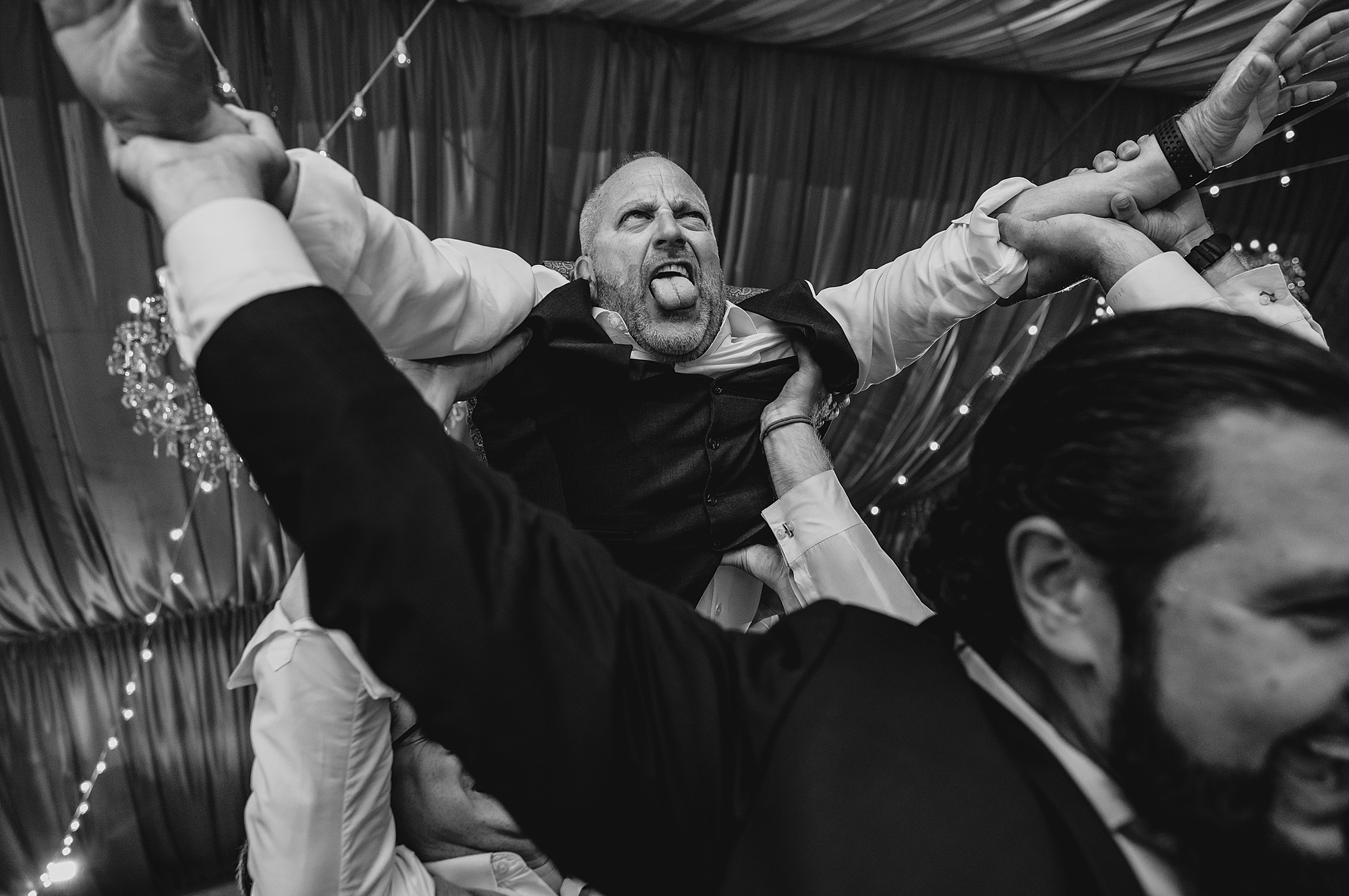 dad of bride jumps on wedding guests holding him in the air