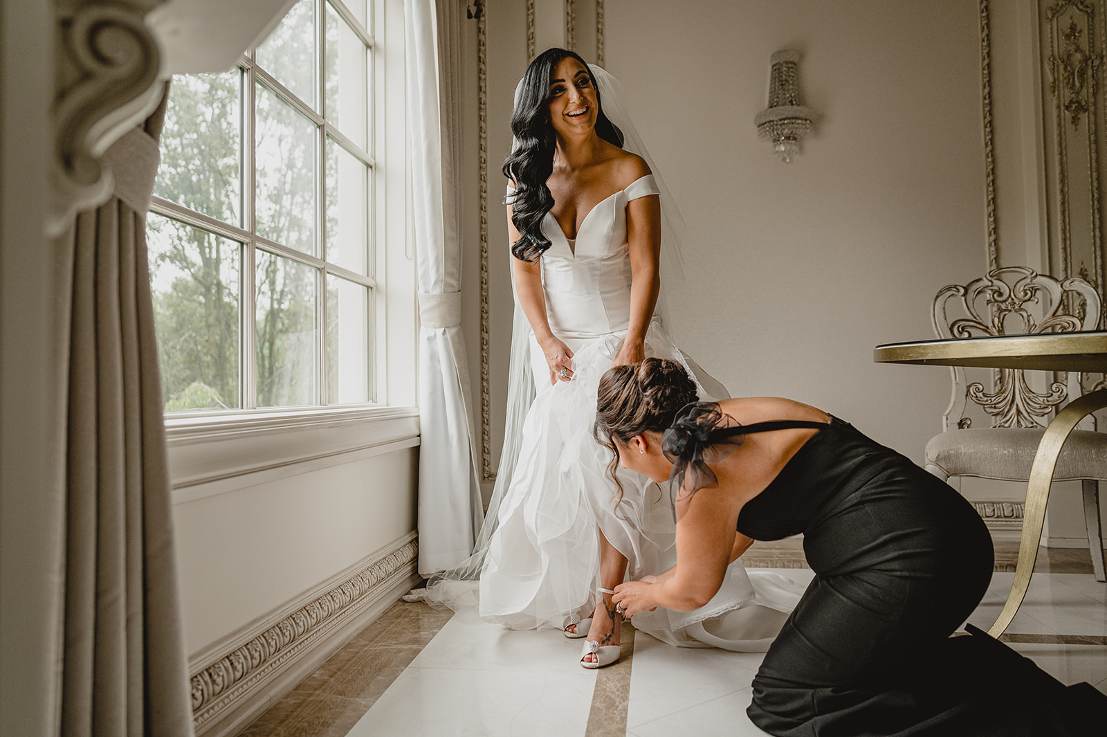 bridesmaid kneels to help bride with shoes before NJ wedding