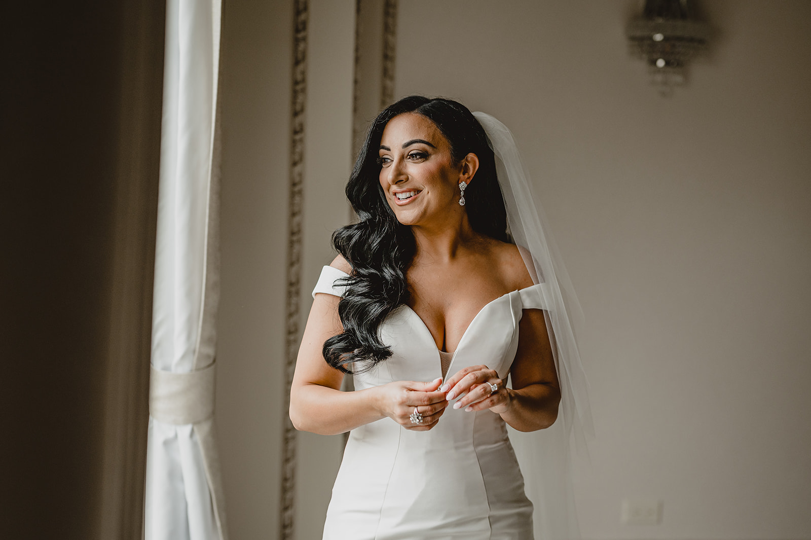 bride smiles holding hands together in front of her wedding gown