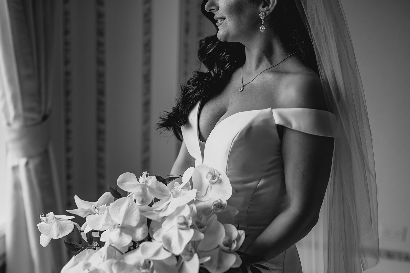 bride smiles in off the shoulder gown with white bouquet of orchids