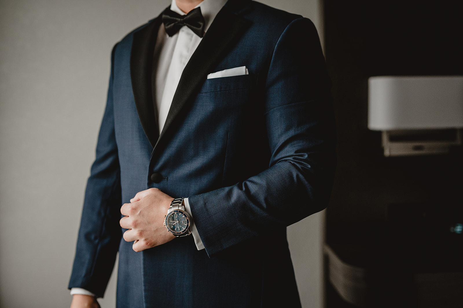 groom holds black lapel on navy suit in hotel room