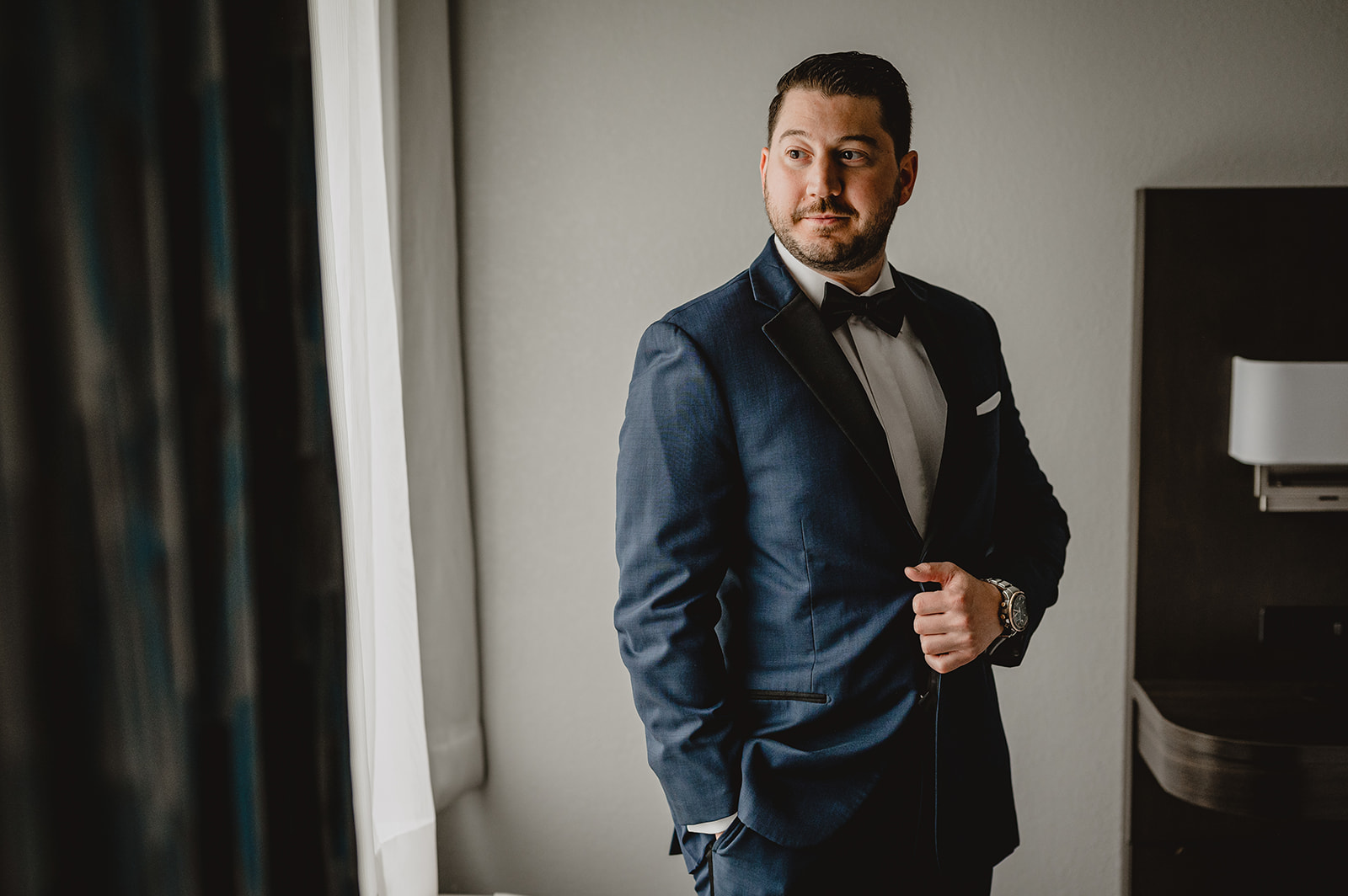 groom holds the black lapel of his navy suit