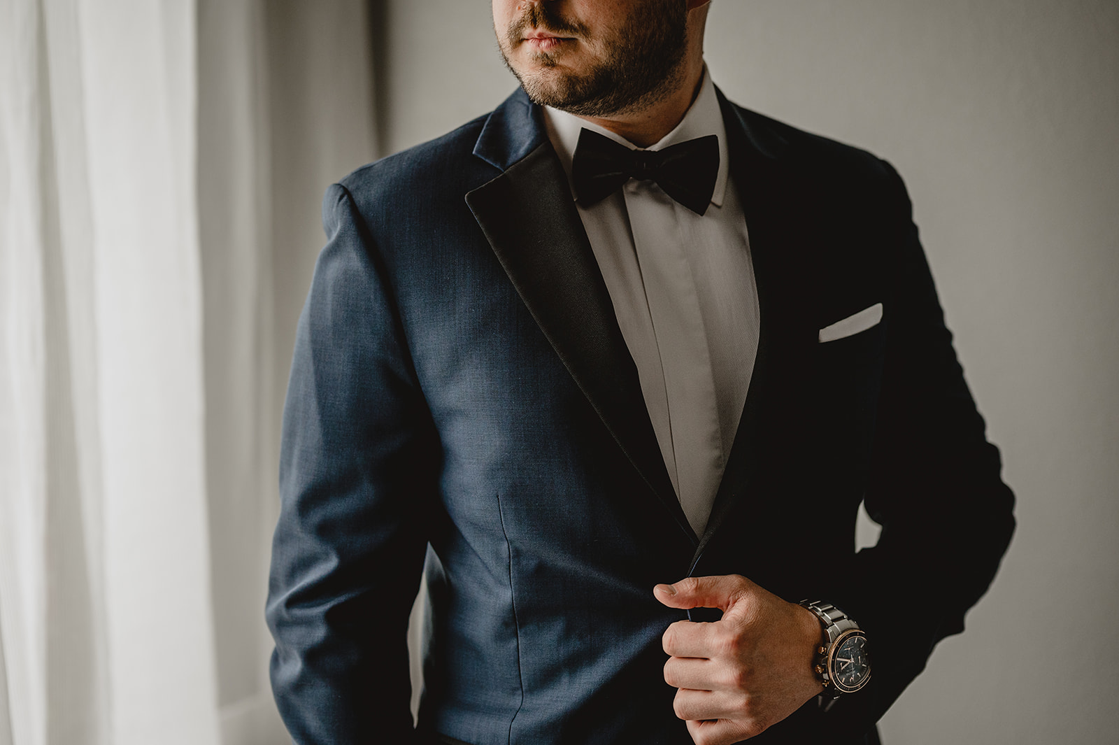 groom stands holding black lapel and buttons of navy suit