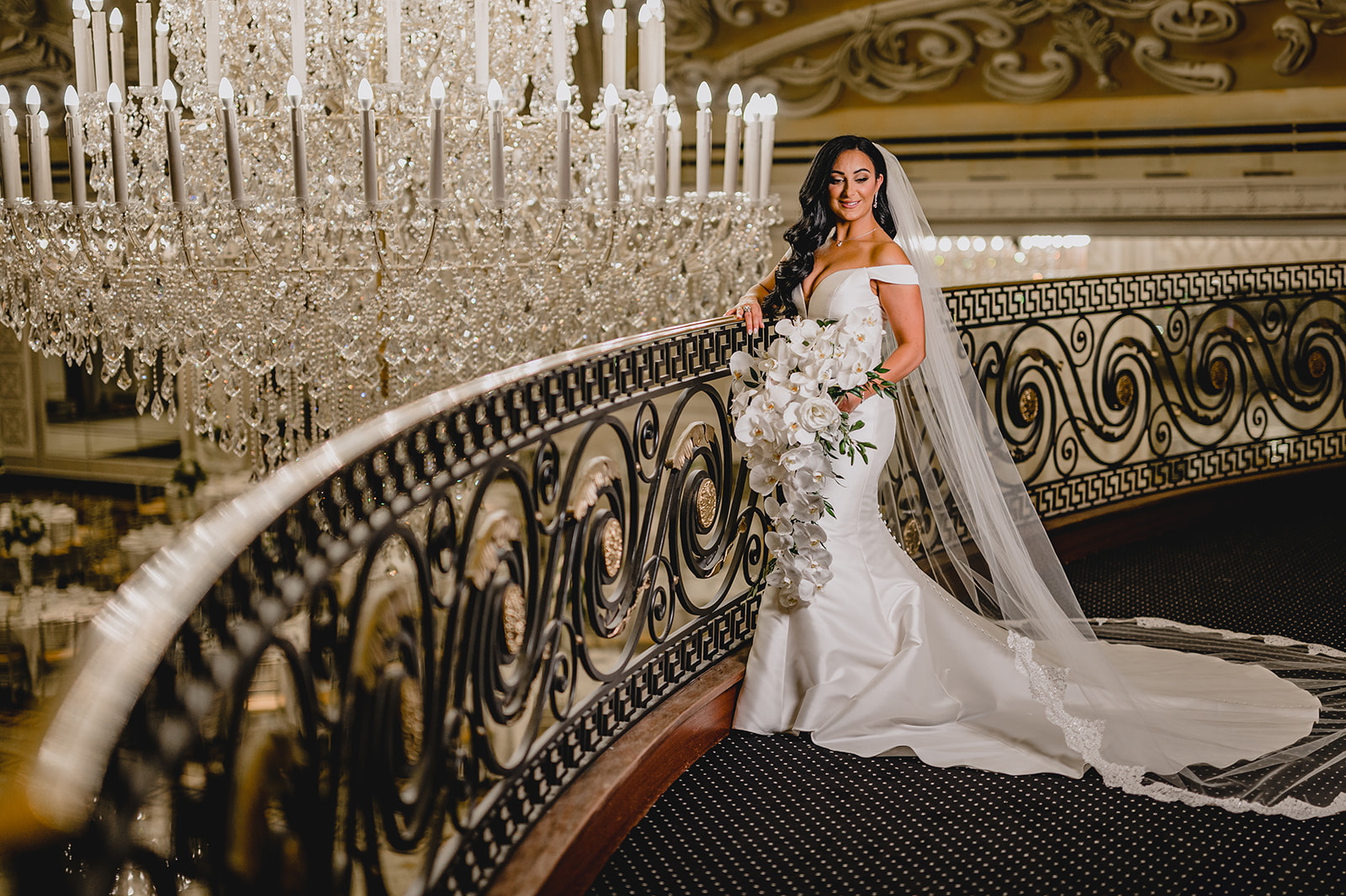 bride holds bouquet of cascading white orchids standing n staircase inside the Venetian