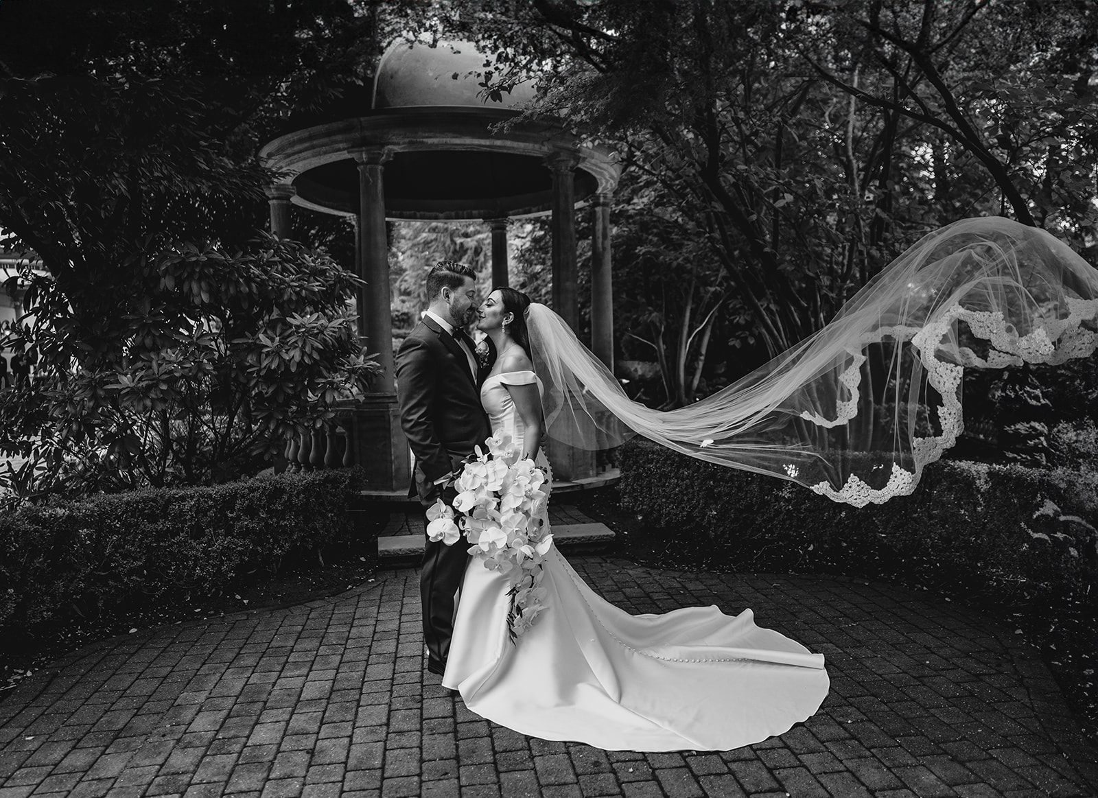 bride and groom hug by gazebo at the Venetian with bride's veil floating behind them