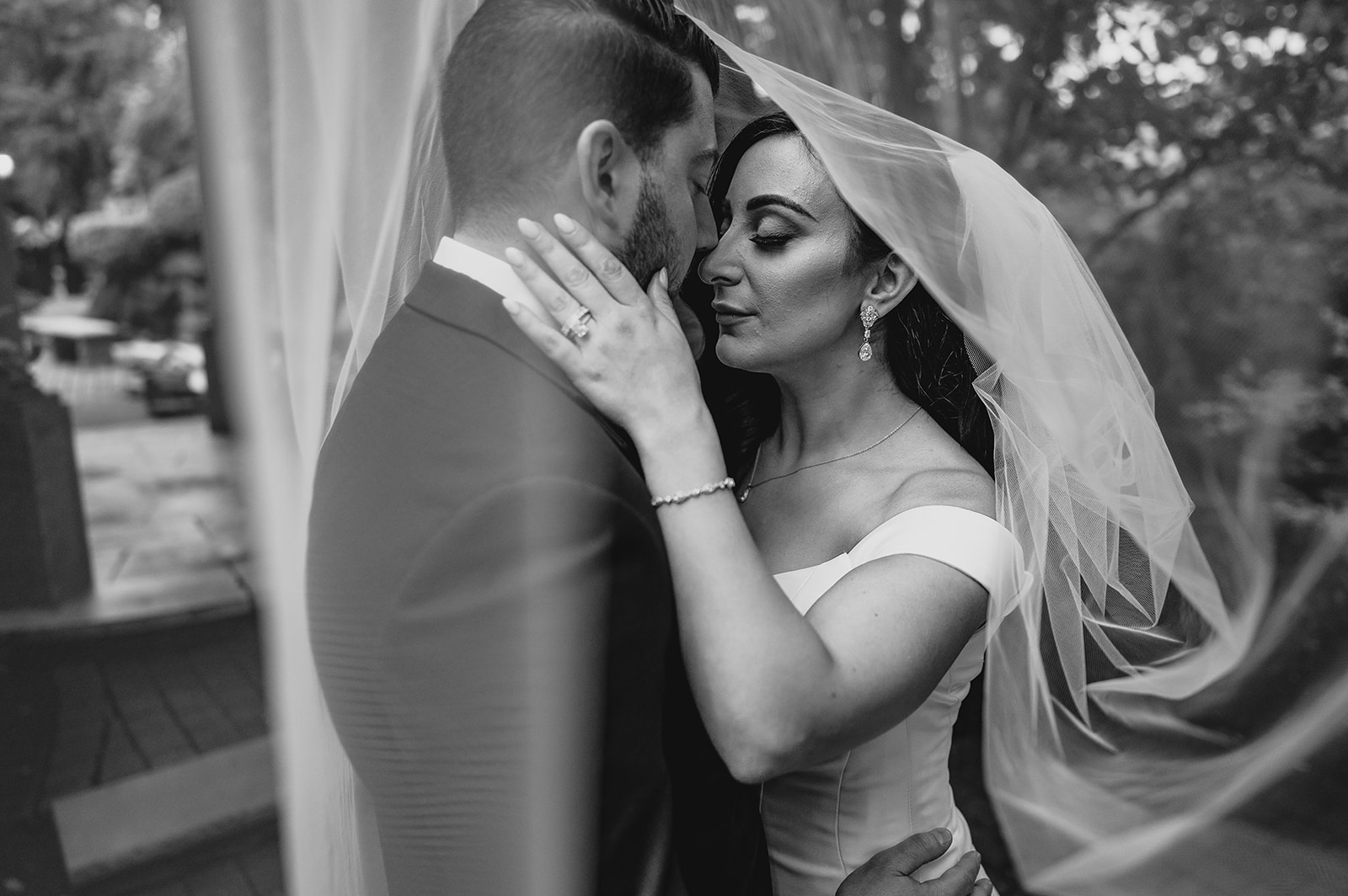 bride holds groom's neck leaning to kiss him under her veil