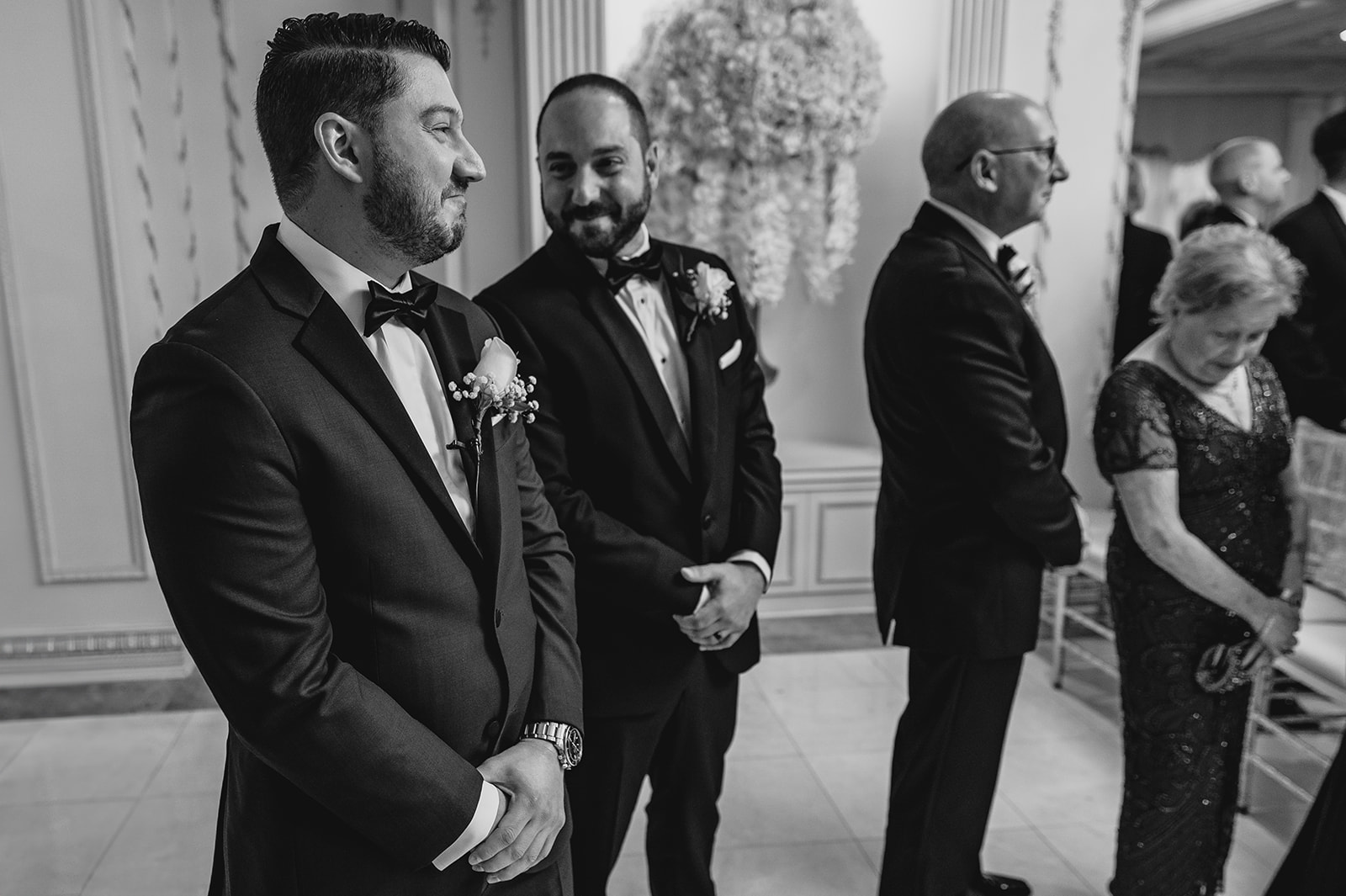 groom watches bride walk down aisle talking to groomsmen 
