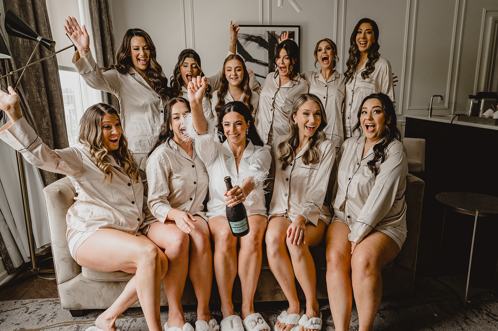 bridesmaids in matching ivory pajamas toast with champagne on sofa