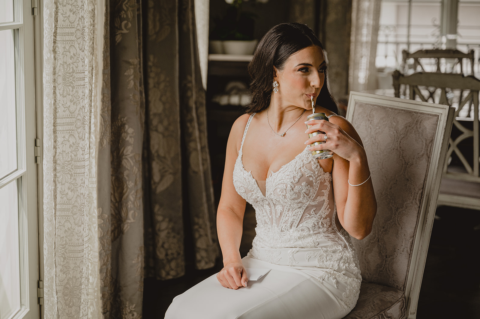 bride drinks champagne out of a straw in tan and white chair