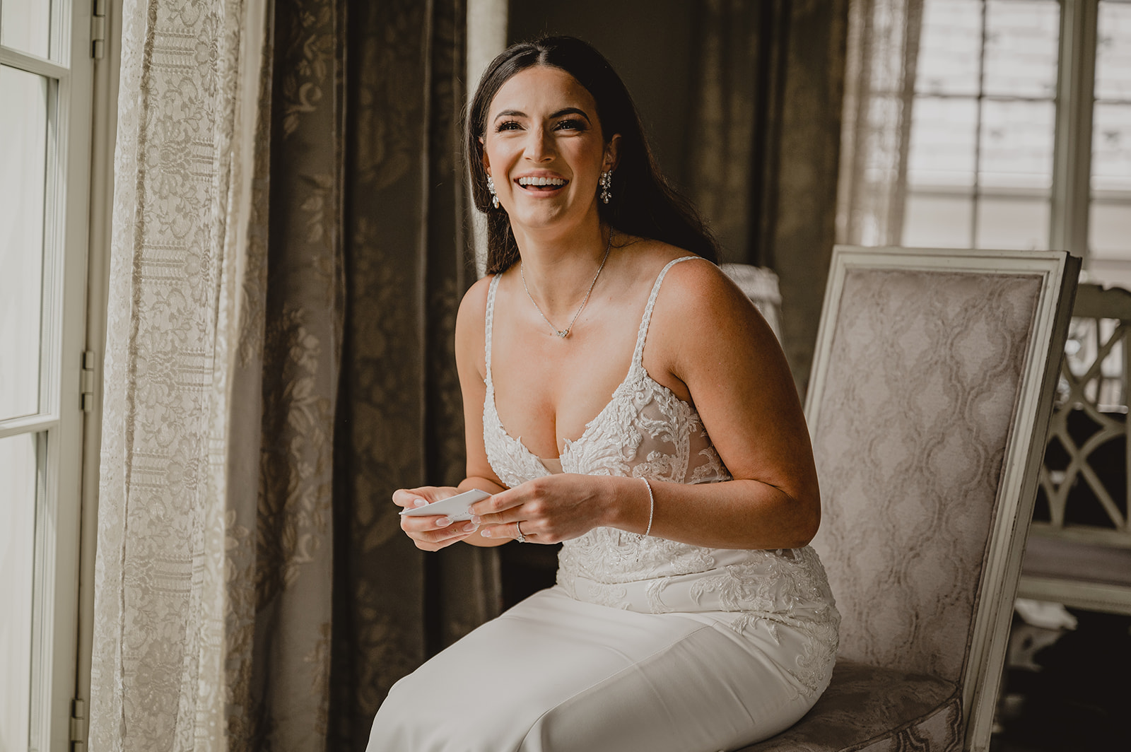bride leans forward laughing reading letter in chair at Park Chateau Estate
