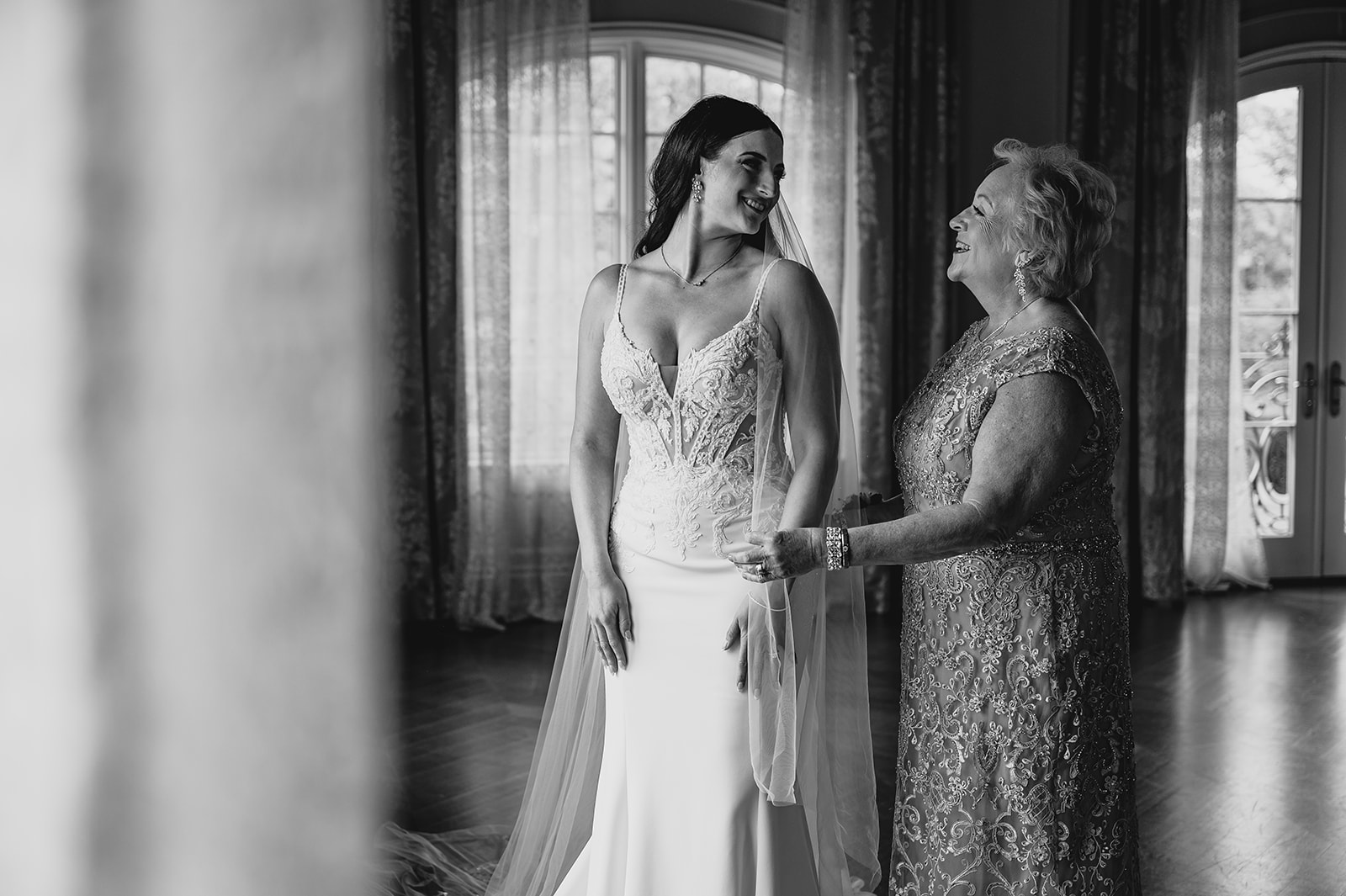 mother looks at bride adjusting veil in bridal suite 