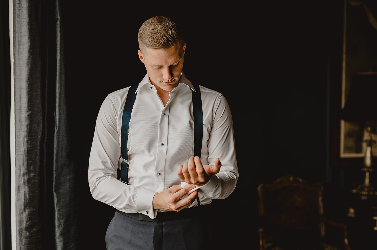 groom stands in suspenders adjusting cufflinks